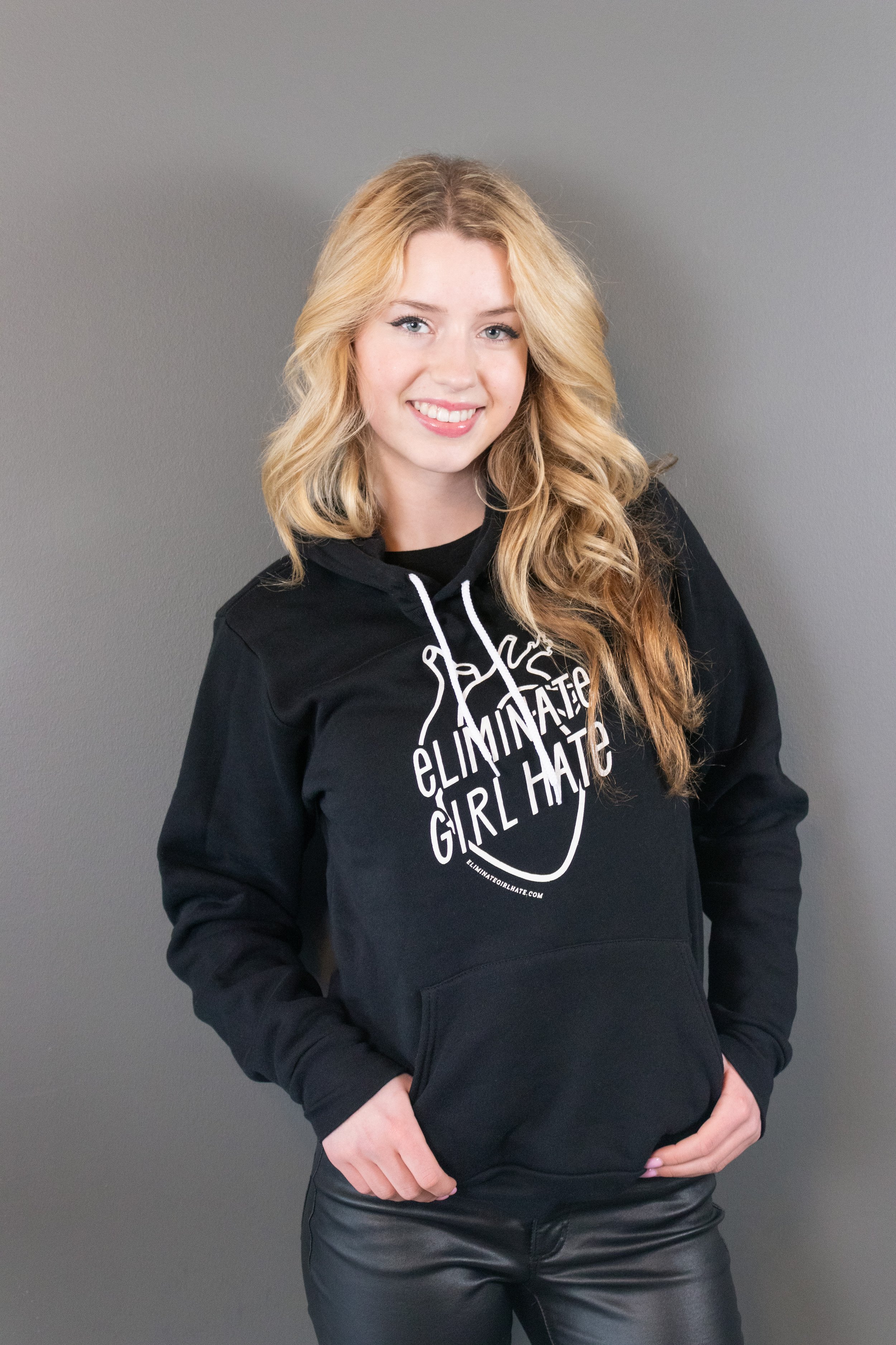 Young woman smiling and wearing the Eliminate Girl Hate unisex hoodie