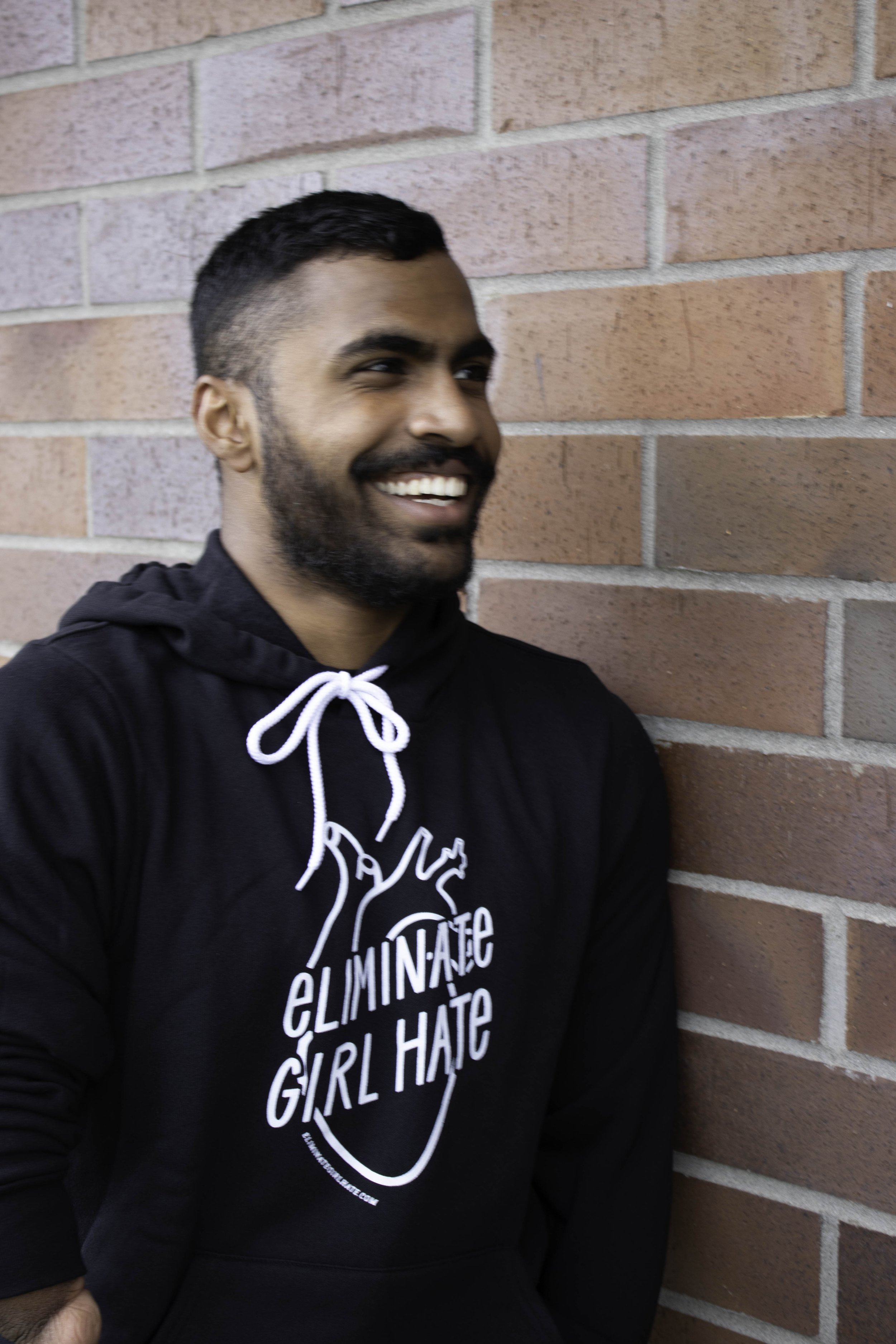 Young man smiling and wearing the Eliminate Girl Hate unisex hoodie