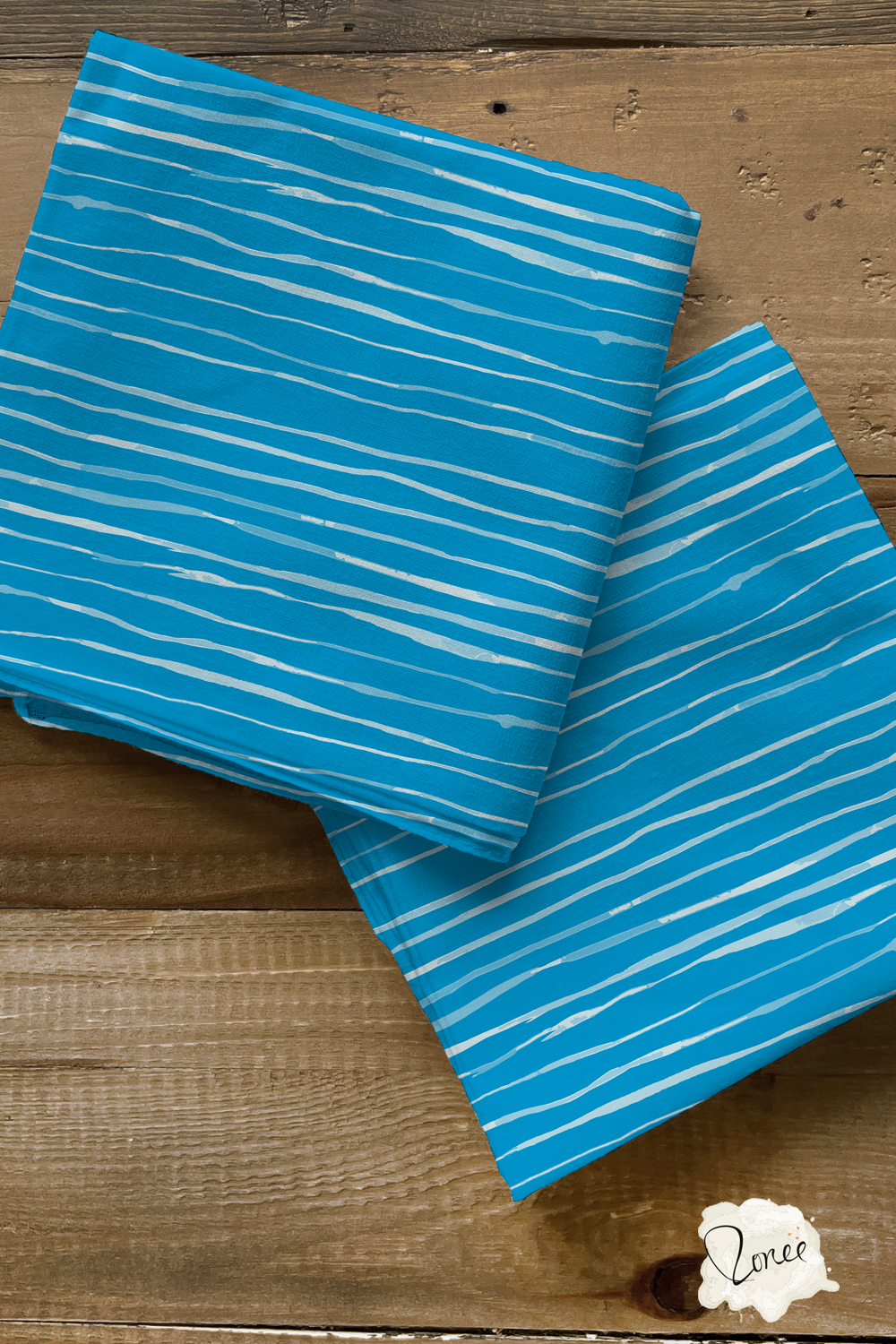 Two folded squares of quilting cotton with a coastal blue organic stripe pattern sit on a rustic wood surface.