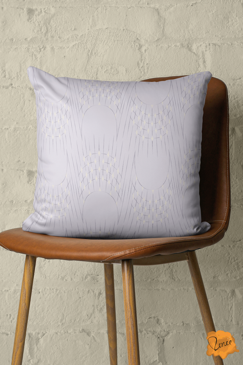 Throw pillow with delicate art deco arches and radisnt starburst lines with sparkling cream diamonds on pale lavender sits on a vintage and leather chair in front of a painted brick wall.