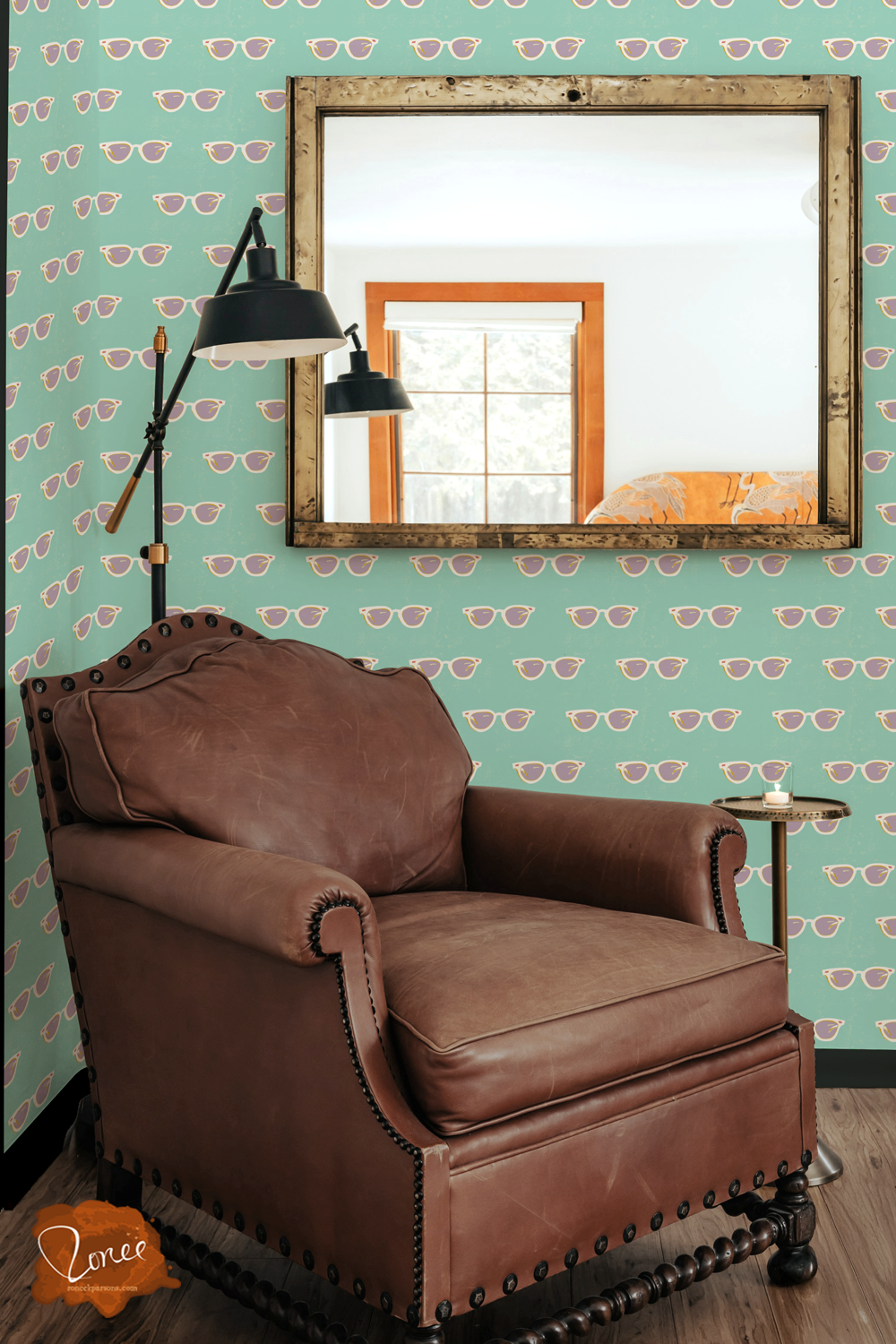 Old leather chair with a black floor lamp and vintage mirror in a room with tuquoise wallpaper with a retro pattern of popart white cateye glases.