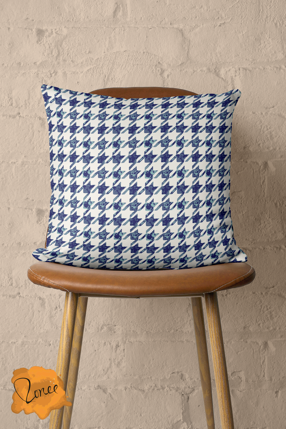 Throw pillow with a navy blue and white houndstooth pattern, sits on a vintage wood and leather chair in front of a painted brick wall..