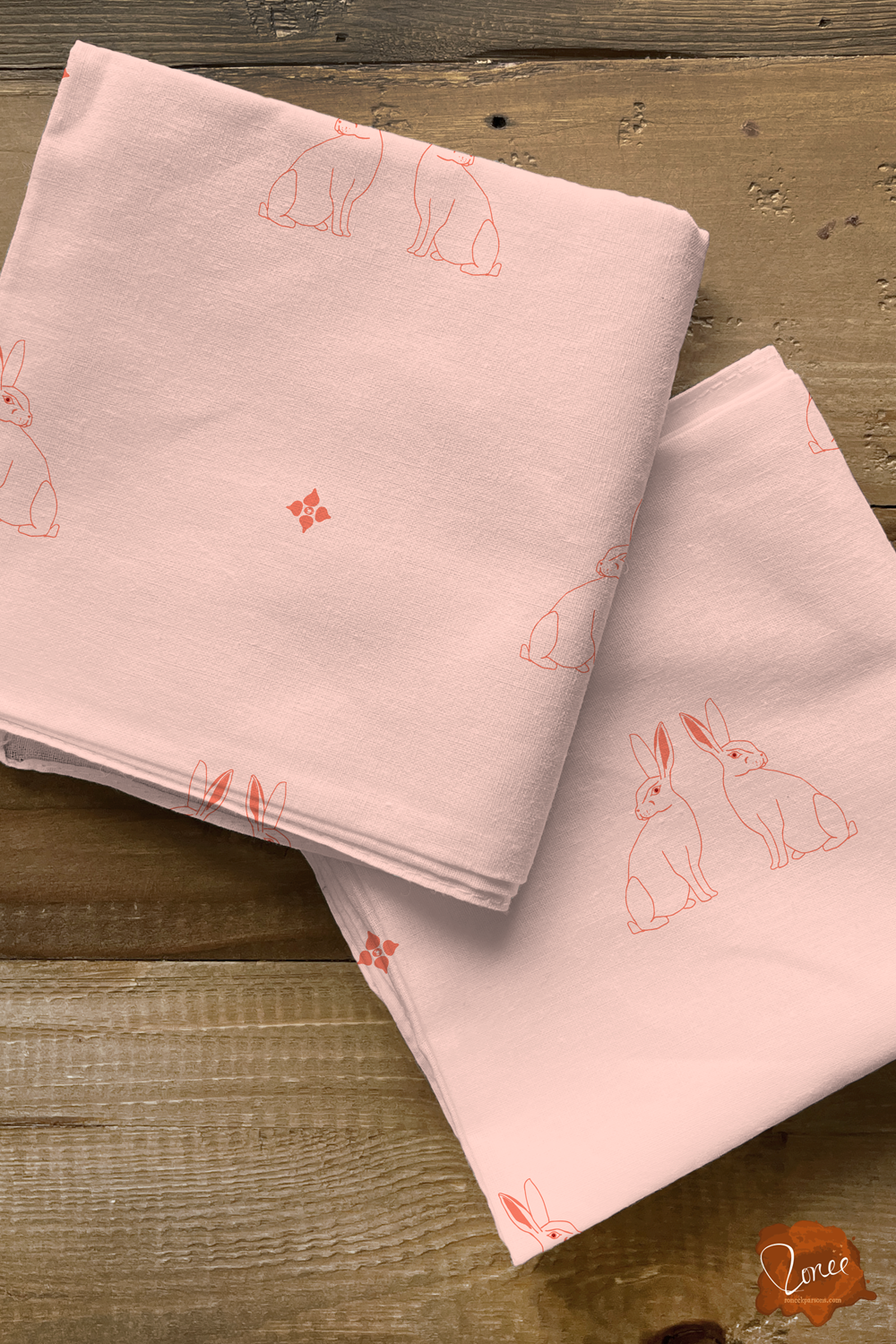 Two squares of folded quilting fabric with pattern of vintage pink line drawn bunnies on white, sitting on an old wood surface.