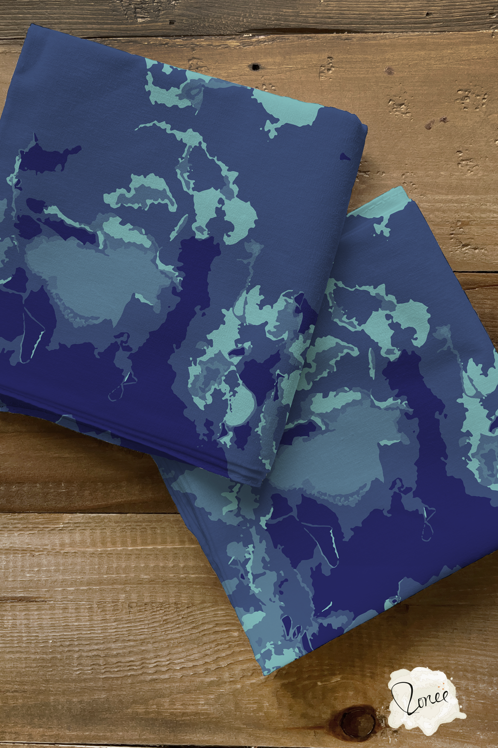 Two squares of folded dark sea blue marbled quilting cotton on an old wood surface.