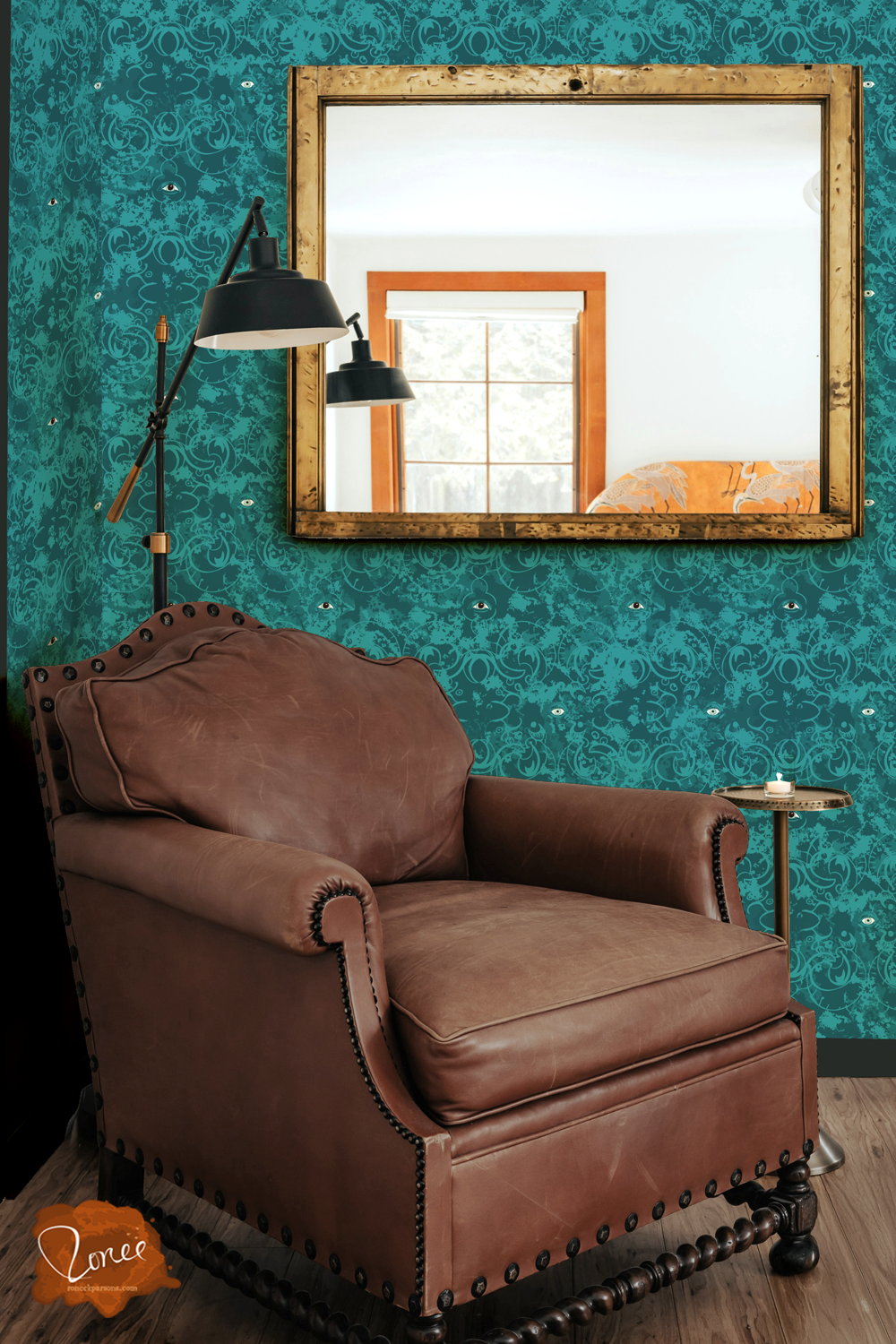 Old leather chair with a black floor lamp and vintage mirror in a room with ornate teal wallpaper dotted with spooky gothic eyes.