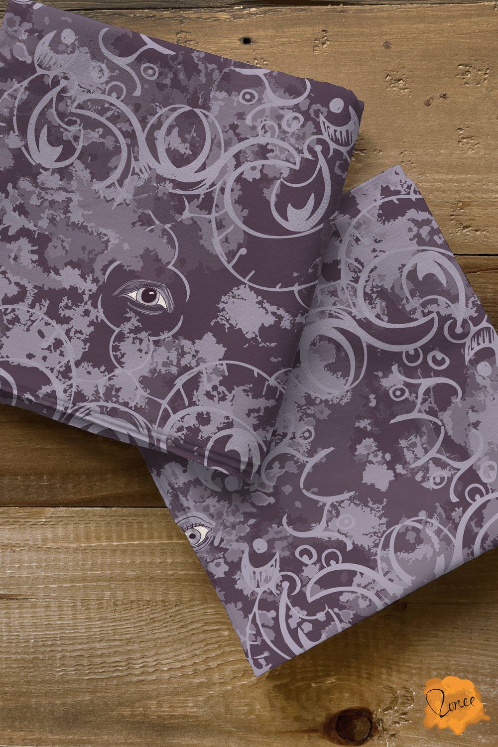 Two squares of folded quilting cotton with a mystical gothic eyes with ornate filigree in deep purple, rest on an old wood surface.