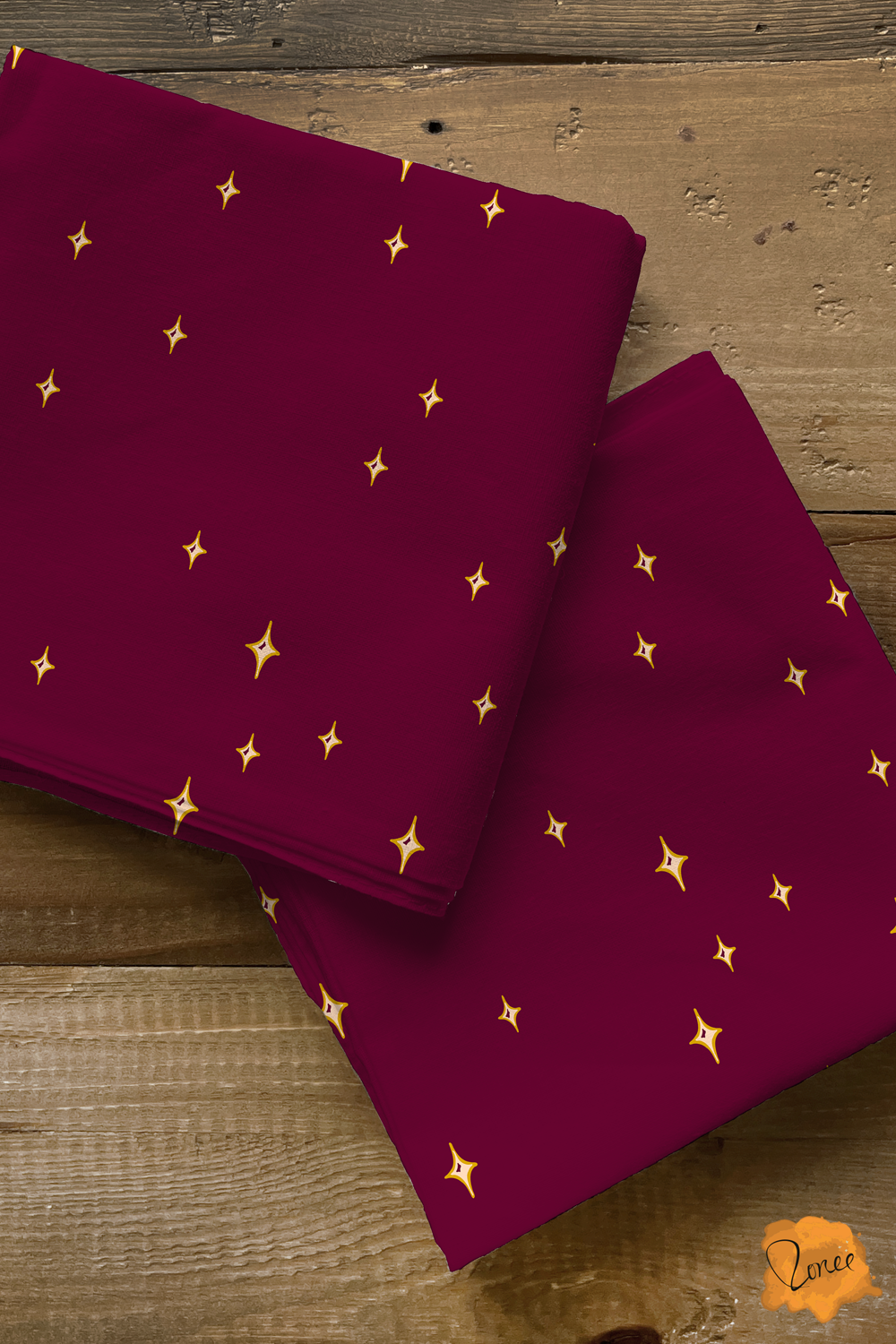 Two squares of folded quilting cotton in deep burgundy with scattered yellow gold four pointed stars, rest on an old wood surface..