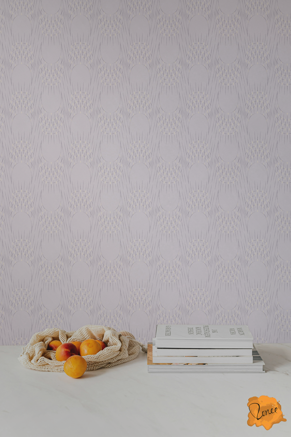 Wallpaper with delicate art deco arches and radisnt starburst lines with sparkling cream diamonds on pale lavender behind a white kitchen counter with a stack of cookbooks and a mesh bag spilling oranges.