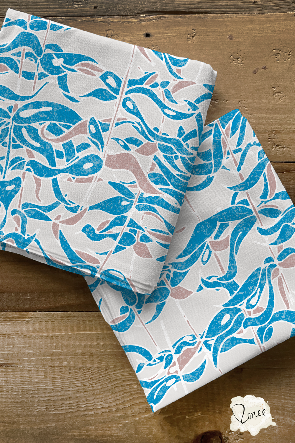 Two folded squares of quilting cotton with a blue and gray seaweed pattern sit on a rustic wood surface.
