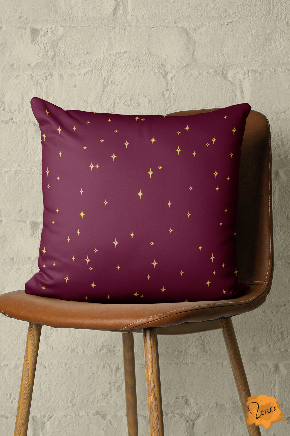 Deep burgundy throw pillow with scattered yellow gold stars sits on a vintage wood and leather chair in front of a painted brick wall.