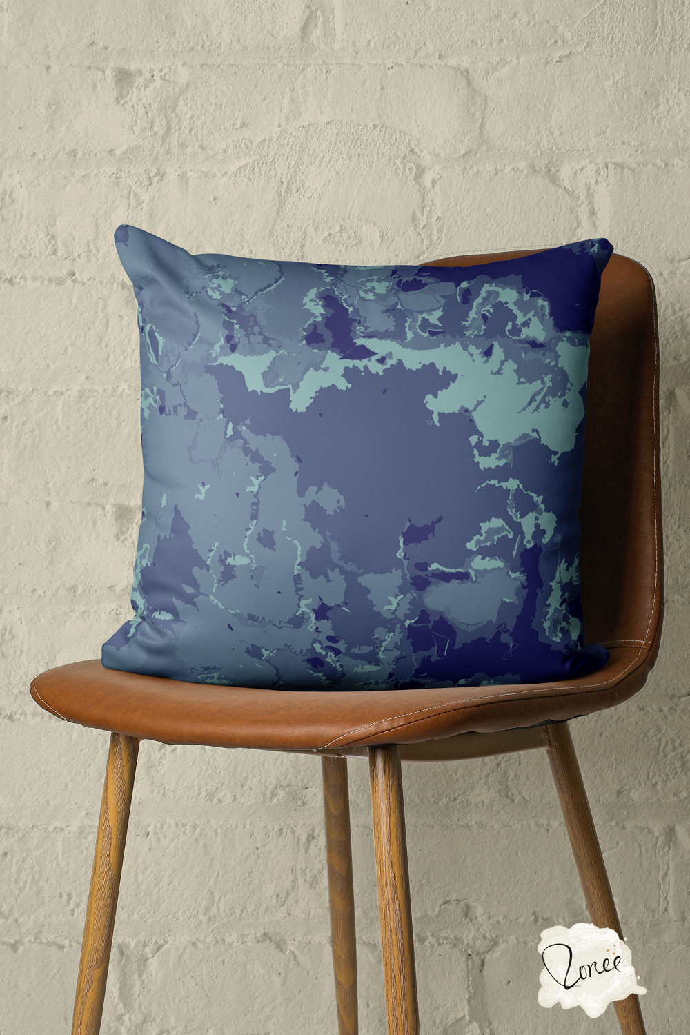 Dark sea blue marbled abstract throw pillow on a vintage wood and leather chair in front of a painted brick wall.