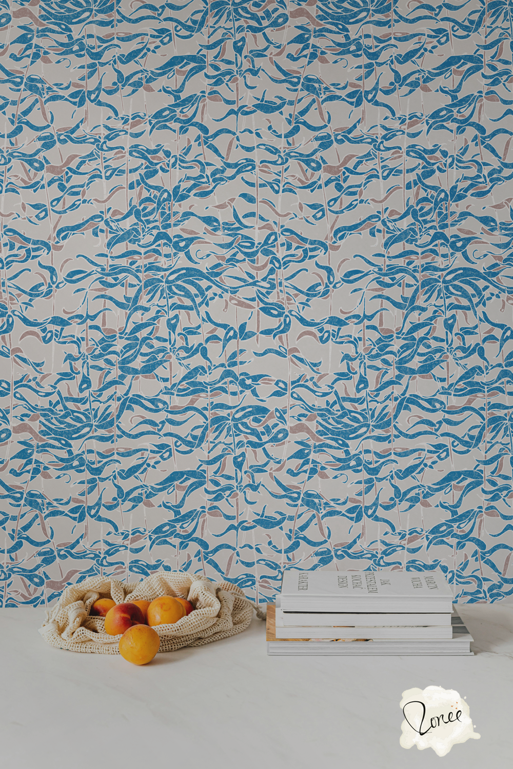 Coastal blue and gray botanical seaweed wallpaper behind a white kitchen counter with a stack of cook books and a mesh bag spilling peaches.