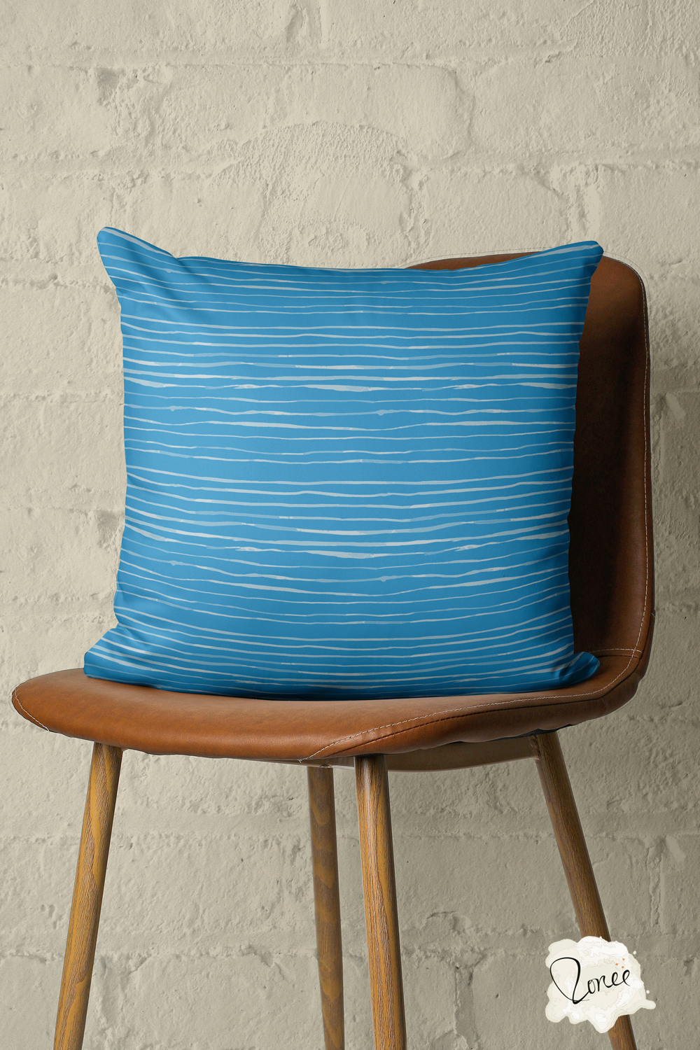 Throw pillow with a coastal blue organic stripes sits on a vintage wood and leather chair with a painted brick wall behind.