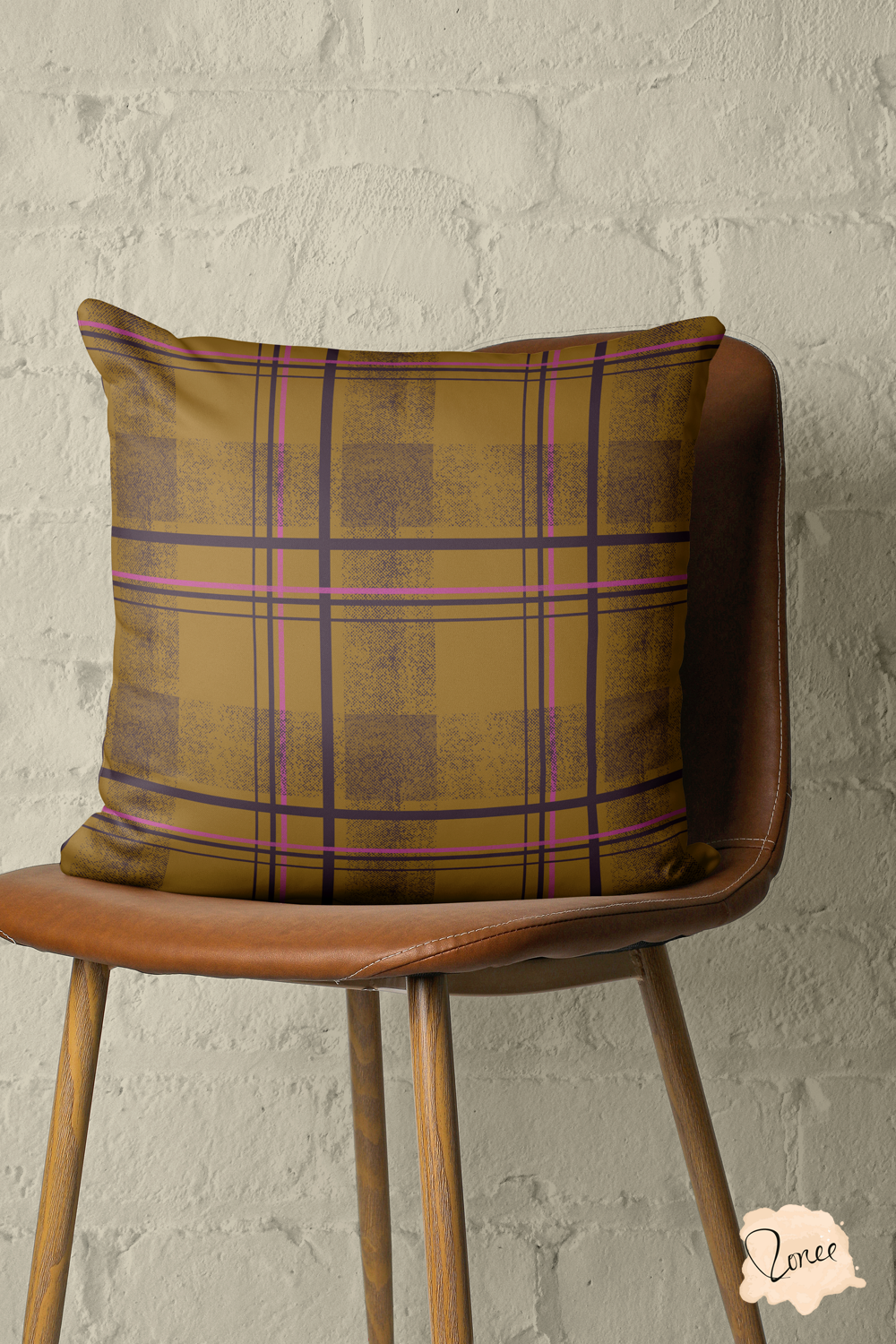 Retro brown and pink plaid patterned throw pillow sits on a vintage wood and leather chair in front of a painted brick wall.