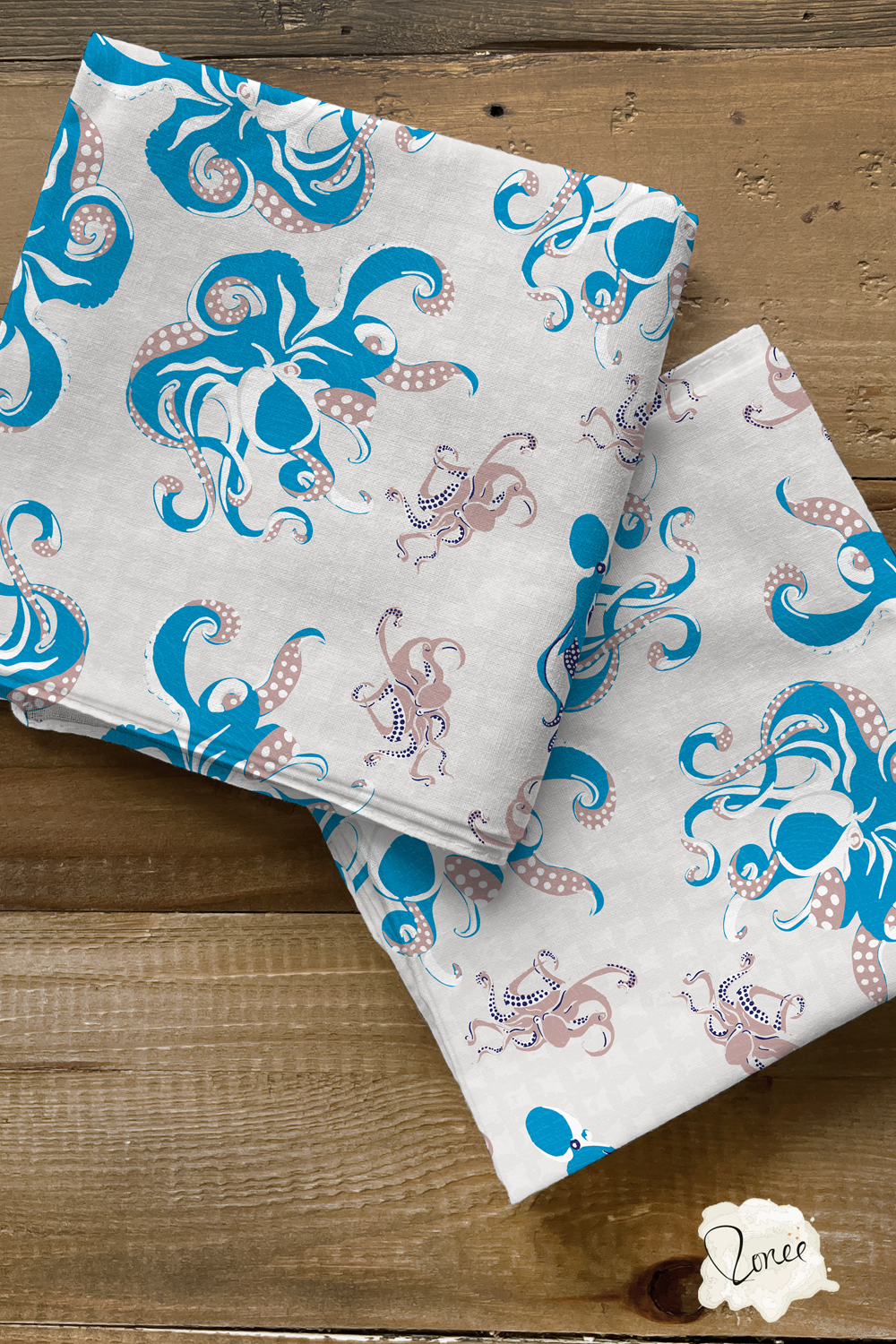 Two squares of folded quilting cotton with blue and taupe octopus and squid on a textured off white background rest on an old wood surface.