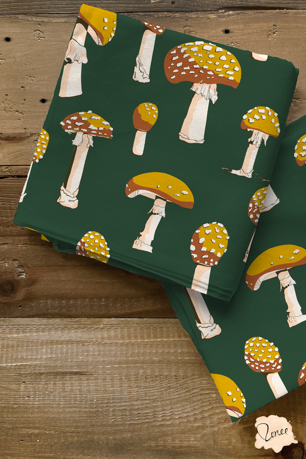 Two pieces of dark green quilting cotton with yellow mushrooms pattern, folded into squares on an old wood surface.