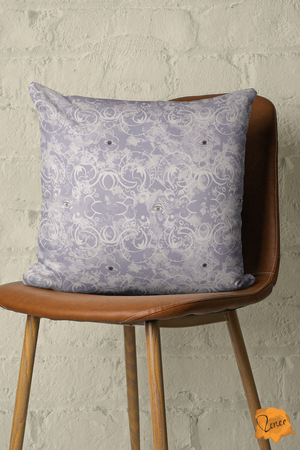 Lavender throw pillow with mystical eyes on an ornate gothic fillagree pattern sits on a vintage and leather chair in front of a painted brick wall.