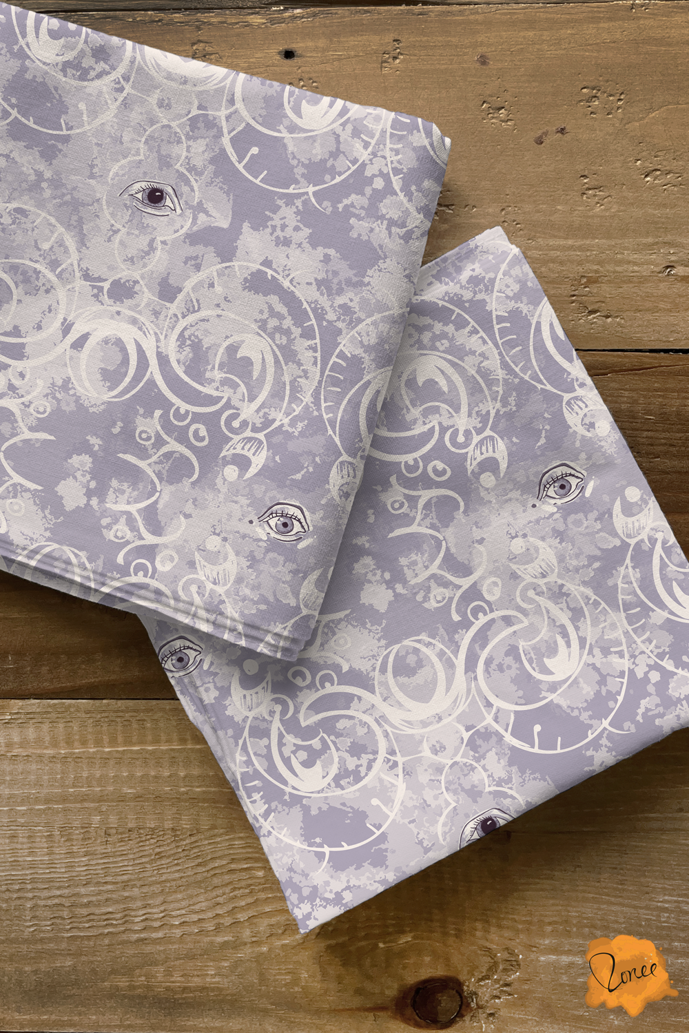 Two squares of folded quilting cotton with a mystical gothic eyes with ornate filigree rest on an old wood surface.