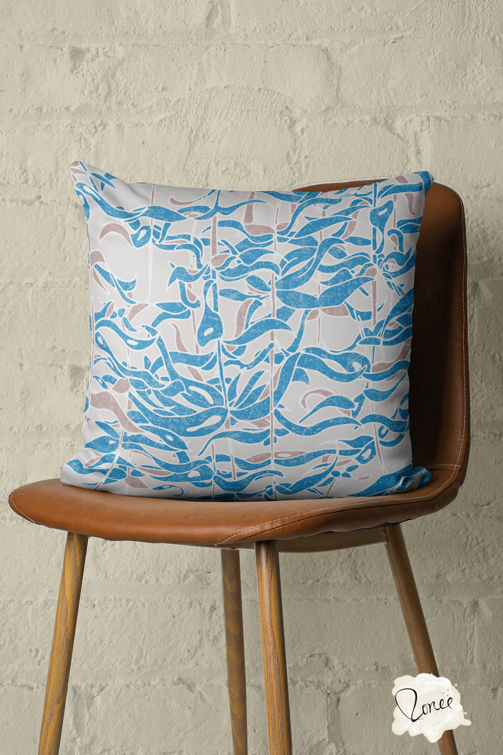 Throw pillow with a blue and gray seaweed botanical pattern sits on a vintage wood and leather chair with a painted brick wall behind.