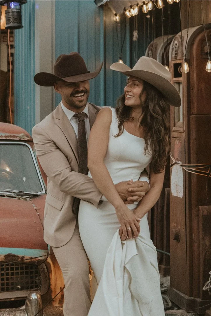 Smiling couple in cowboy hats by an antique car, a sample portrait style at Sparks Museum and Event Center