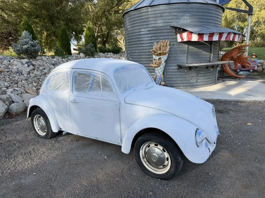 White vintage Volkswagen Beetle parked by a grain silo, a favorite posing spot at Sparks Museum and Event Center