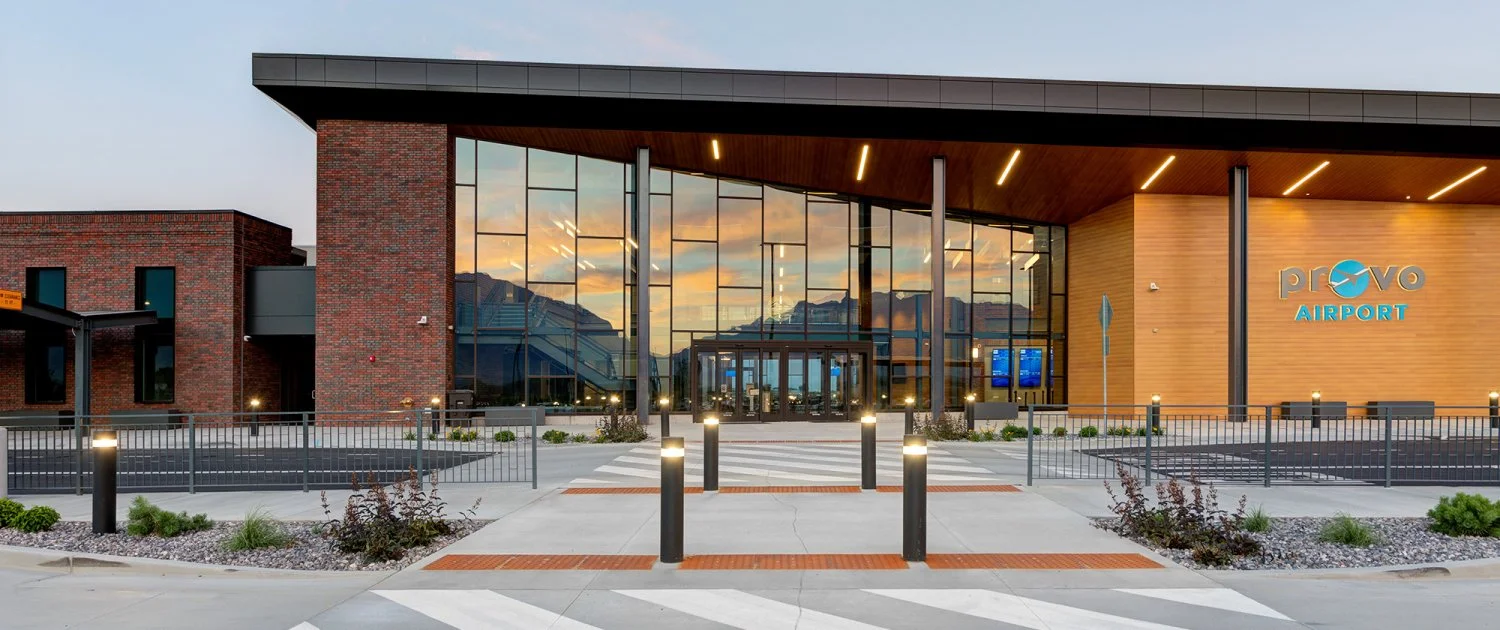 Modern exterior of Provo Airport at sunset, featuring large glass windows, warm wood paneling, and the Provo Airport logo — showcasing small-town charm with big-city design