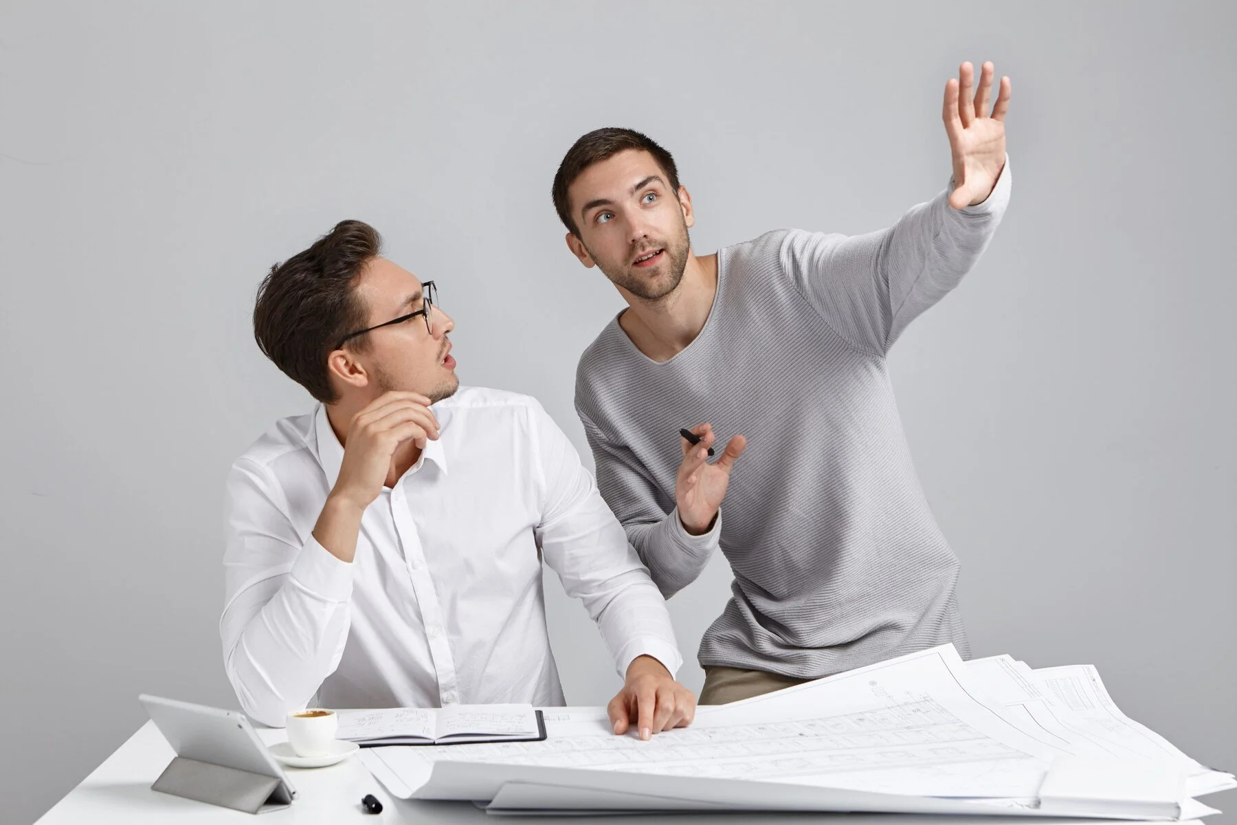 Two men in a meeting, one seated and the other standing and pointing to plans on the table – reflecting Wiseep’s collaborative and strategic approach