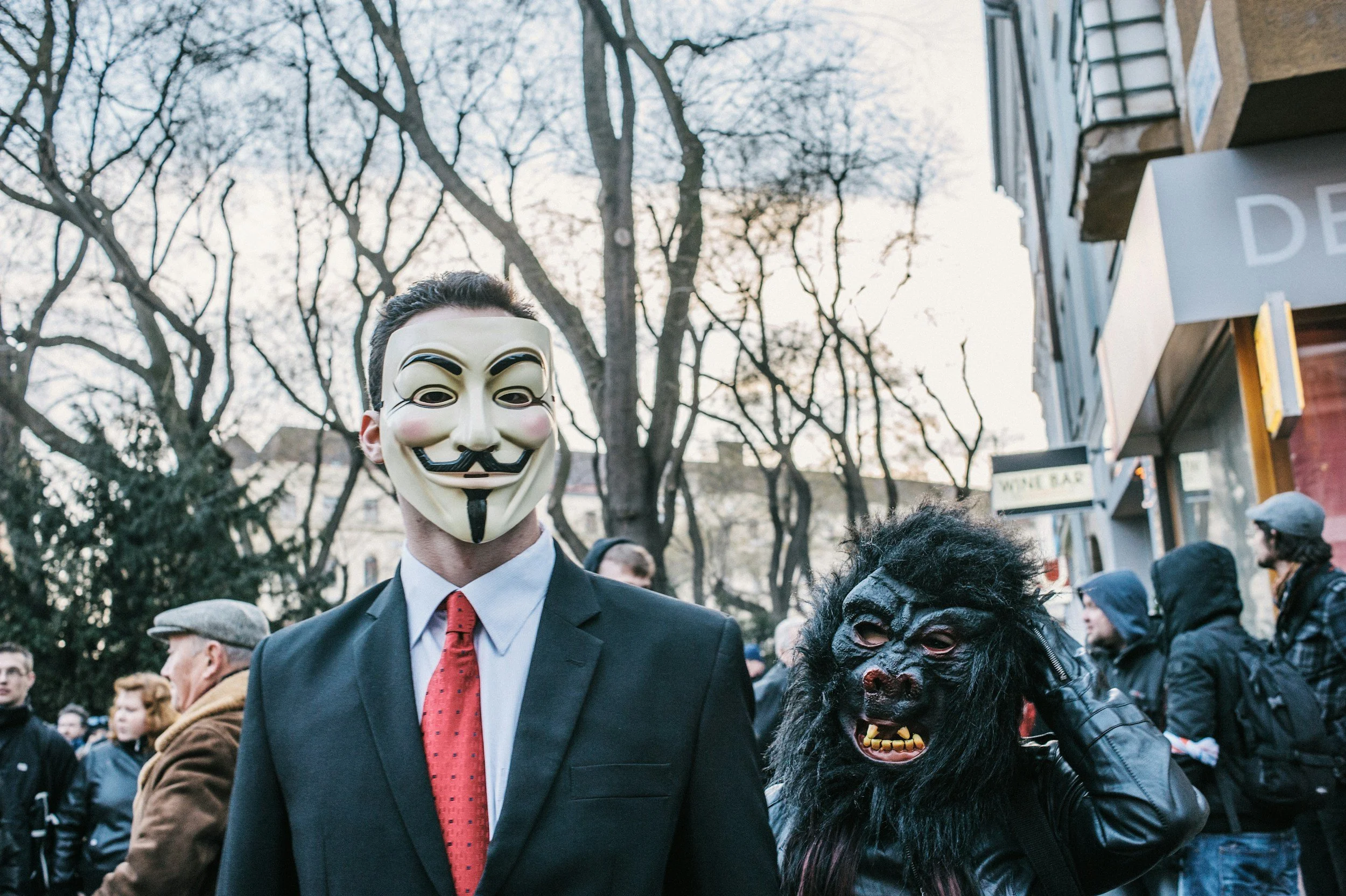 People wearing masks during a street event with leafless trees and buildings in the background.