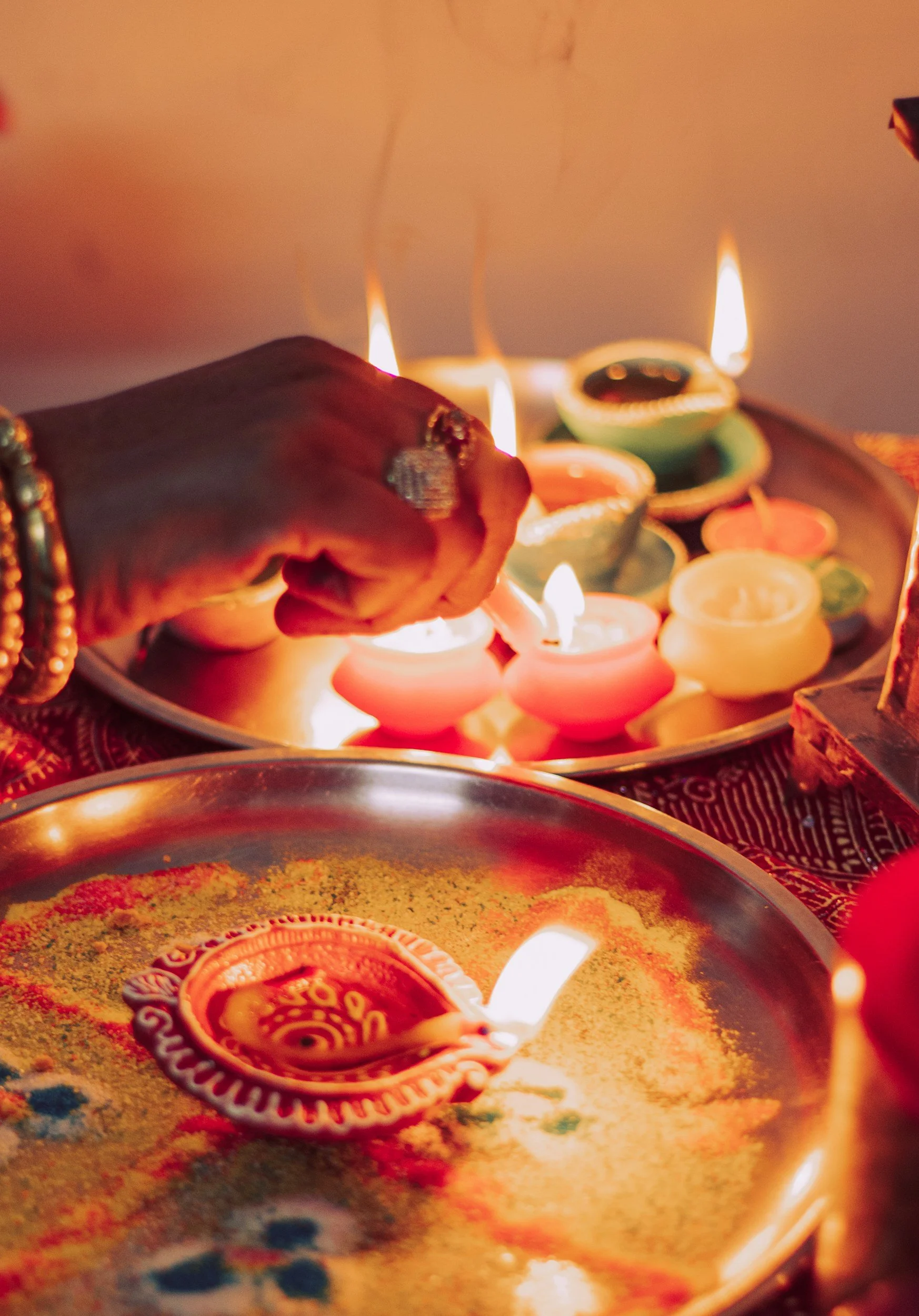 Hand lighting traditional diya lamps during a celebration with multiple lit candles and colorful decorations.