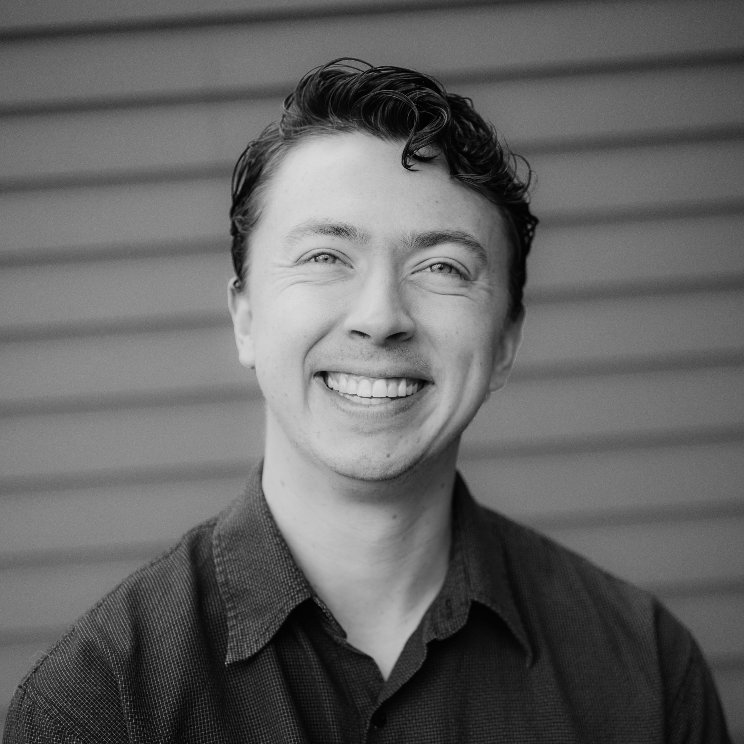 Close-up of a smiling man with curly hair, wearing a checkered shirt, in black and white.