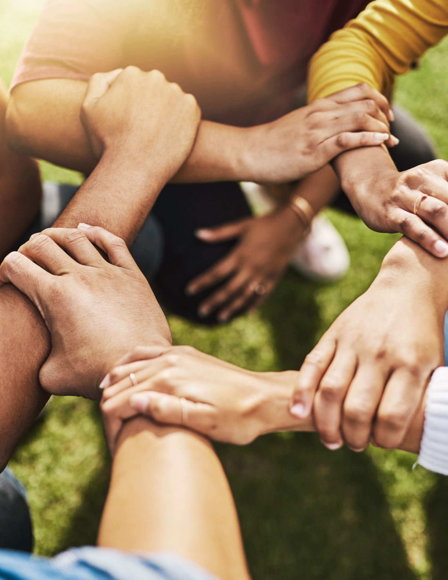 Close-up of diverse hands joining in a circle outdoors, symbolizing teamwork and unity.