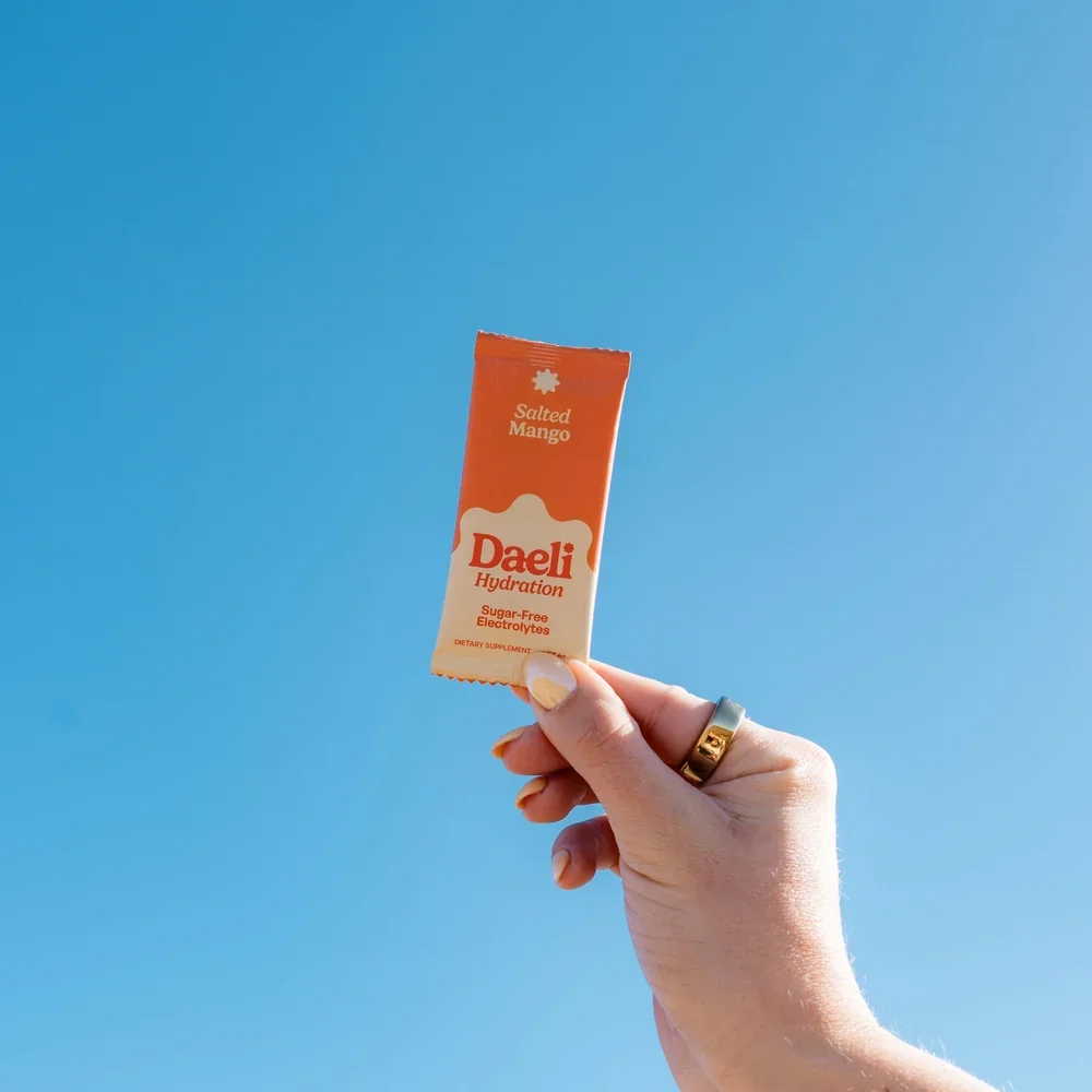 daeli-hydration-salted-mango-electrolyte-sachet-hand-blue-sky.webp