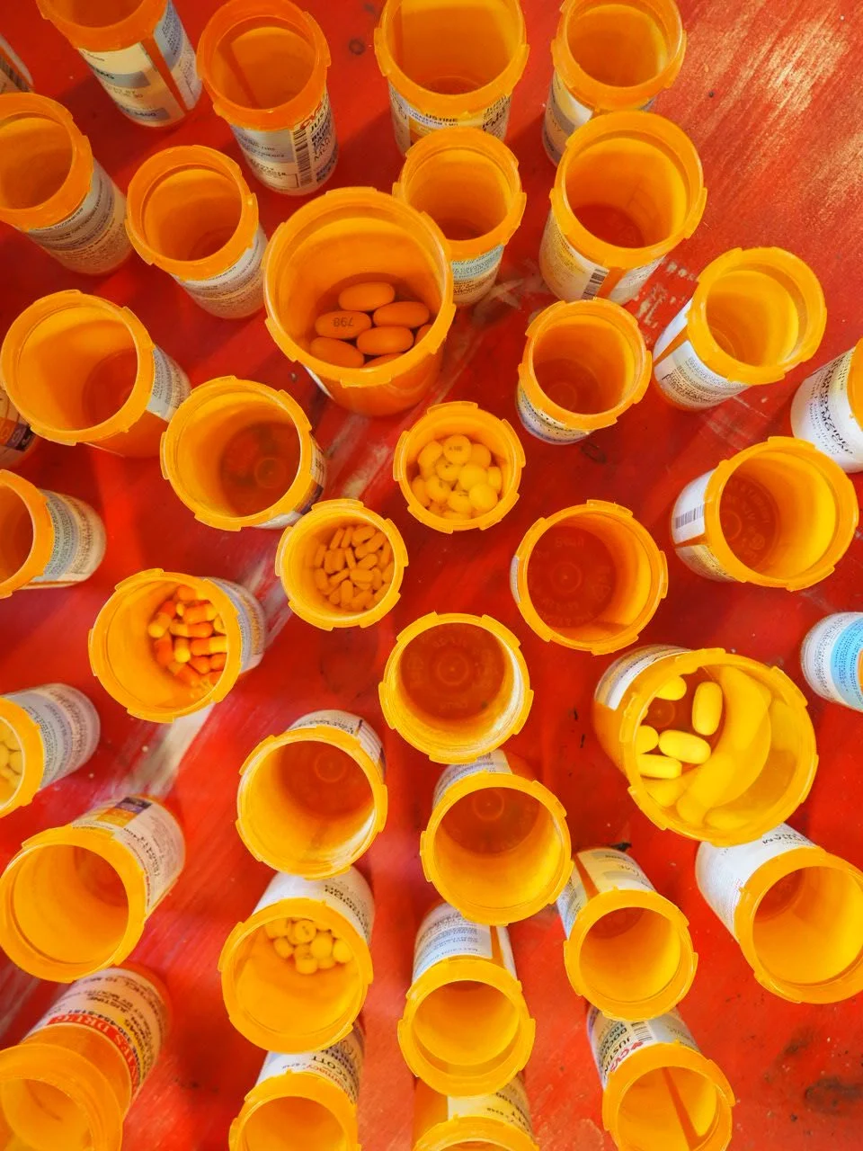 close up of orange pill bottles and some pills, expired medication from decades of medical and psychiatric treatment without lids on