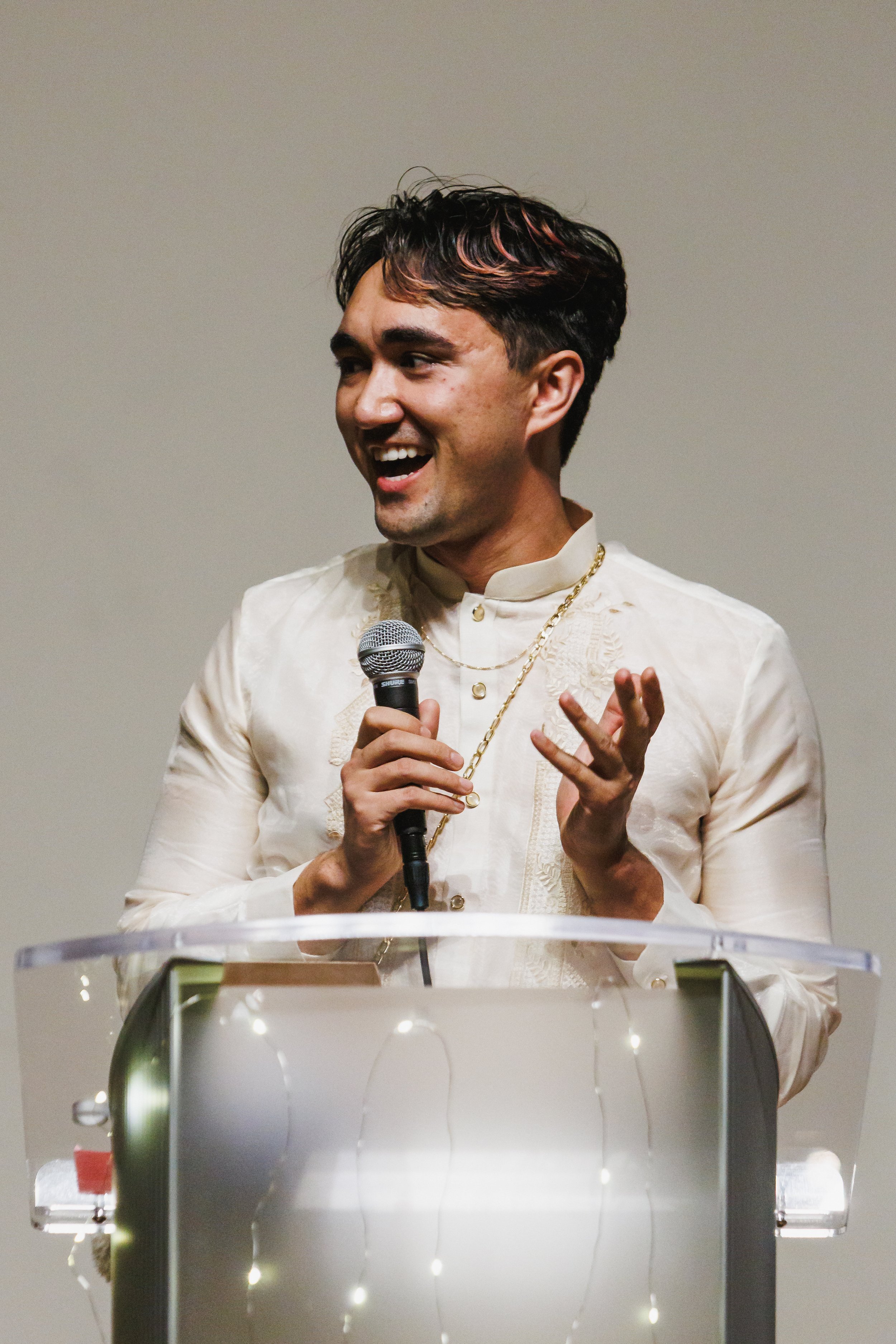 The poet Rob Macaisa Colgate, delighted in front of a podium, in a barong tagalog with golden accessories.