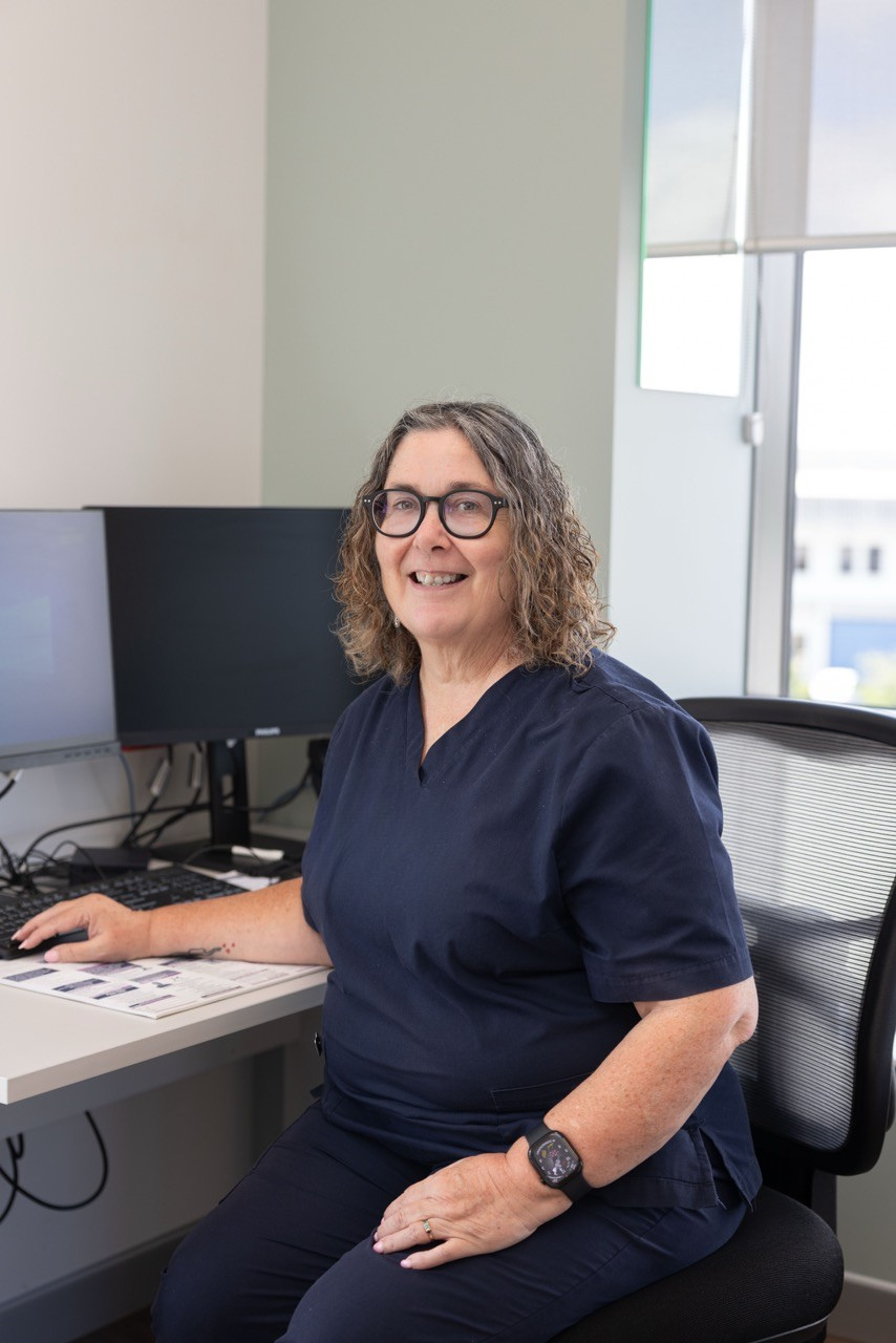Sleep Physiologist Colleen Lockwood sitting at a desk with computer monitors, smiling at the camera.