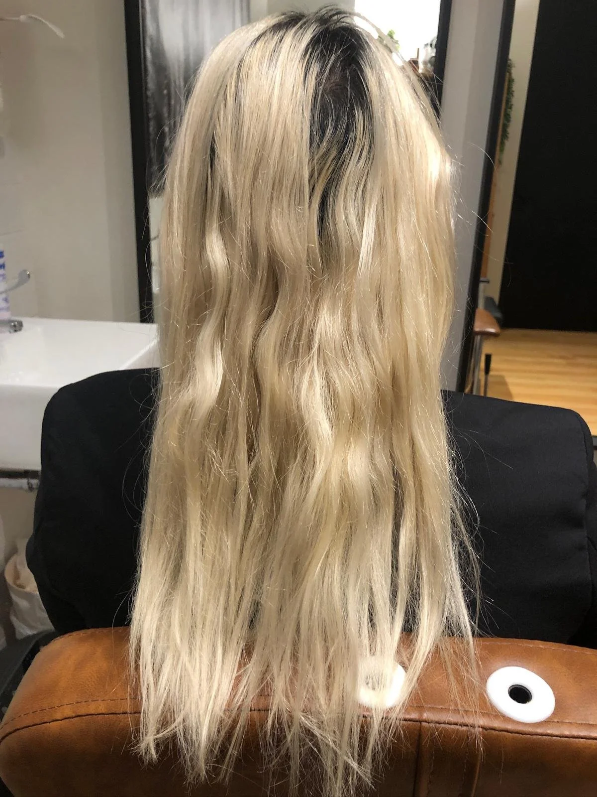 Person with long blonde hair sitting on a brown chair.