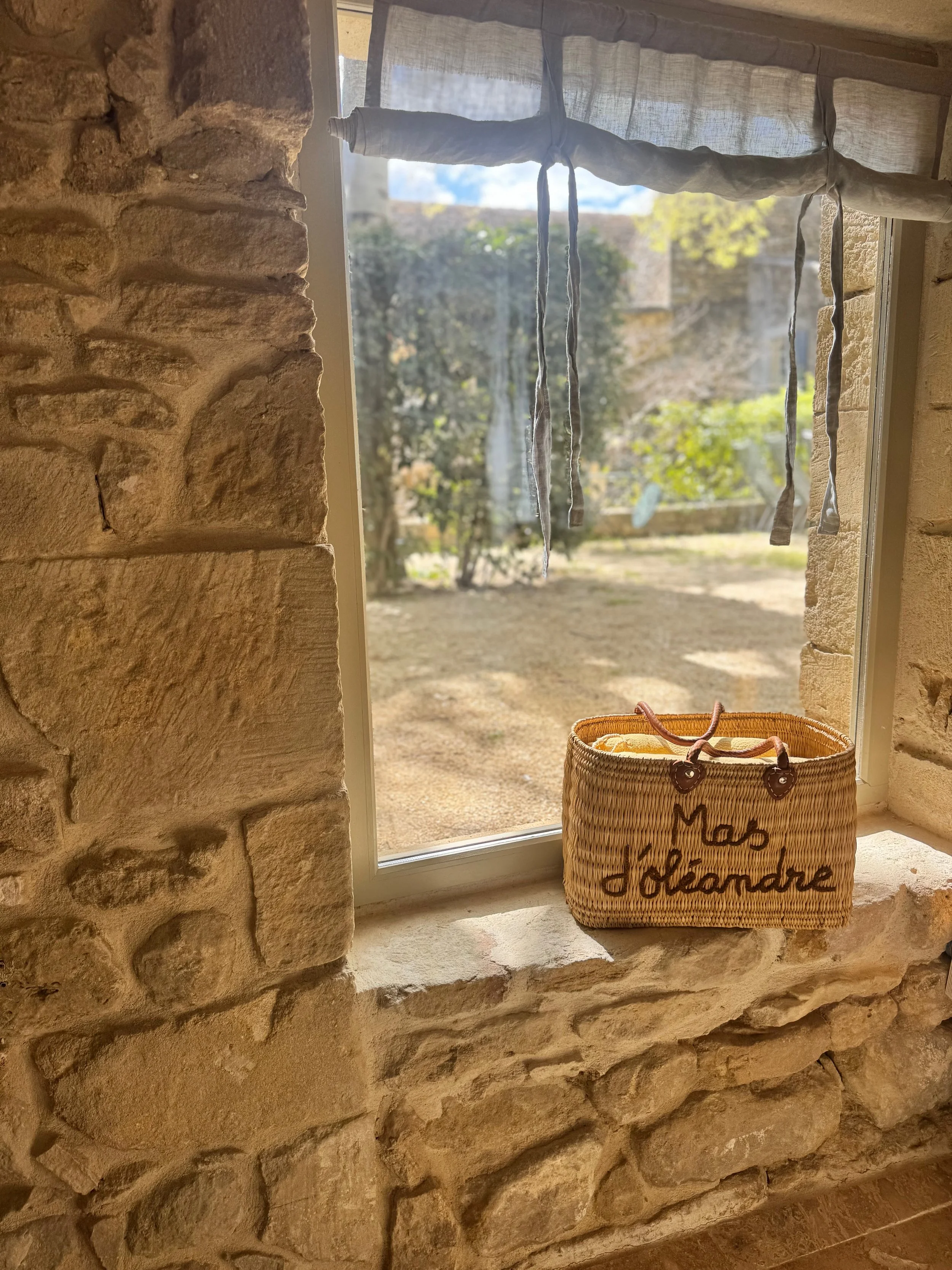 Une fenêtre avec une vue d'un jardin extérieur, un panier en osier avec l'inscription 'Mais découvrir' posé sur le rebord de la fenêtre, et un tissu léger suspendu à la fenêtre.