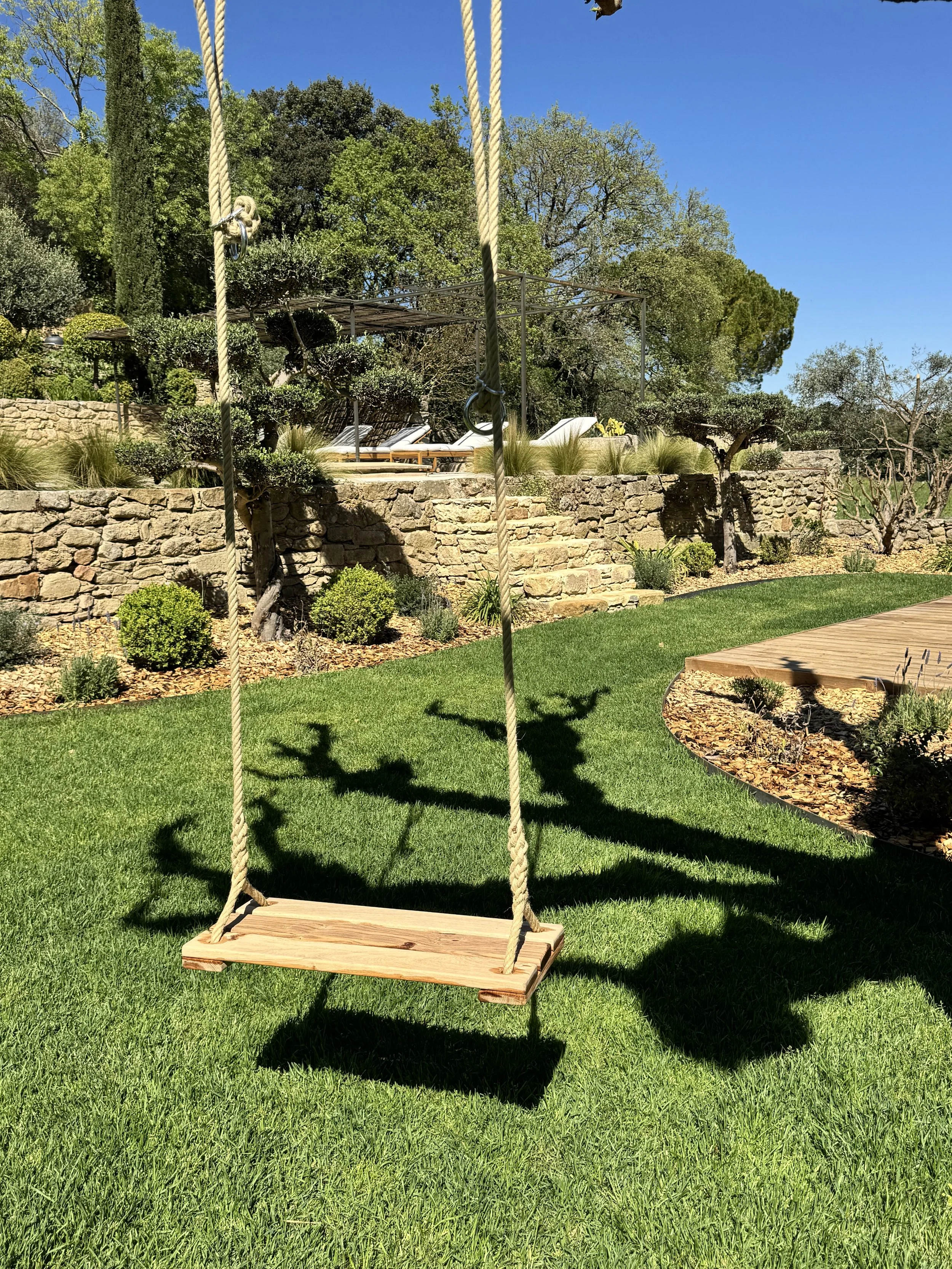 Balancoire en bois suspendue avec des cordes dans un jardin verdoyant ensoleillé.