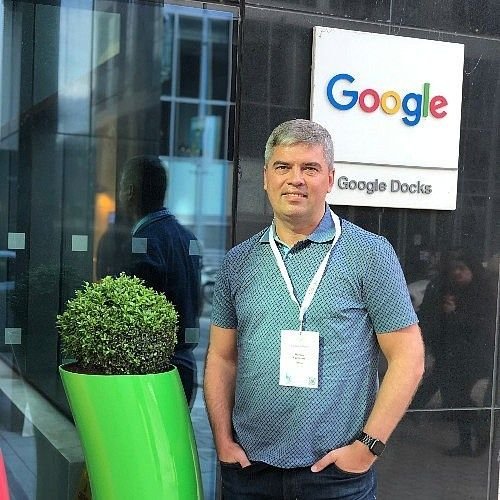 Man standing outside Google office near a Google sign and Google Docs banner.
