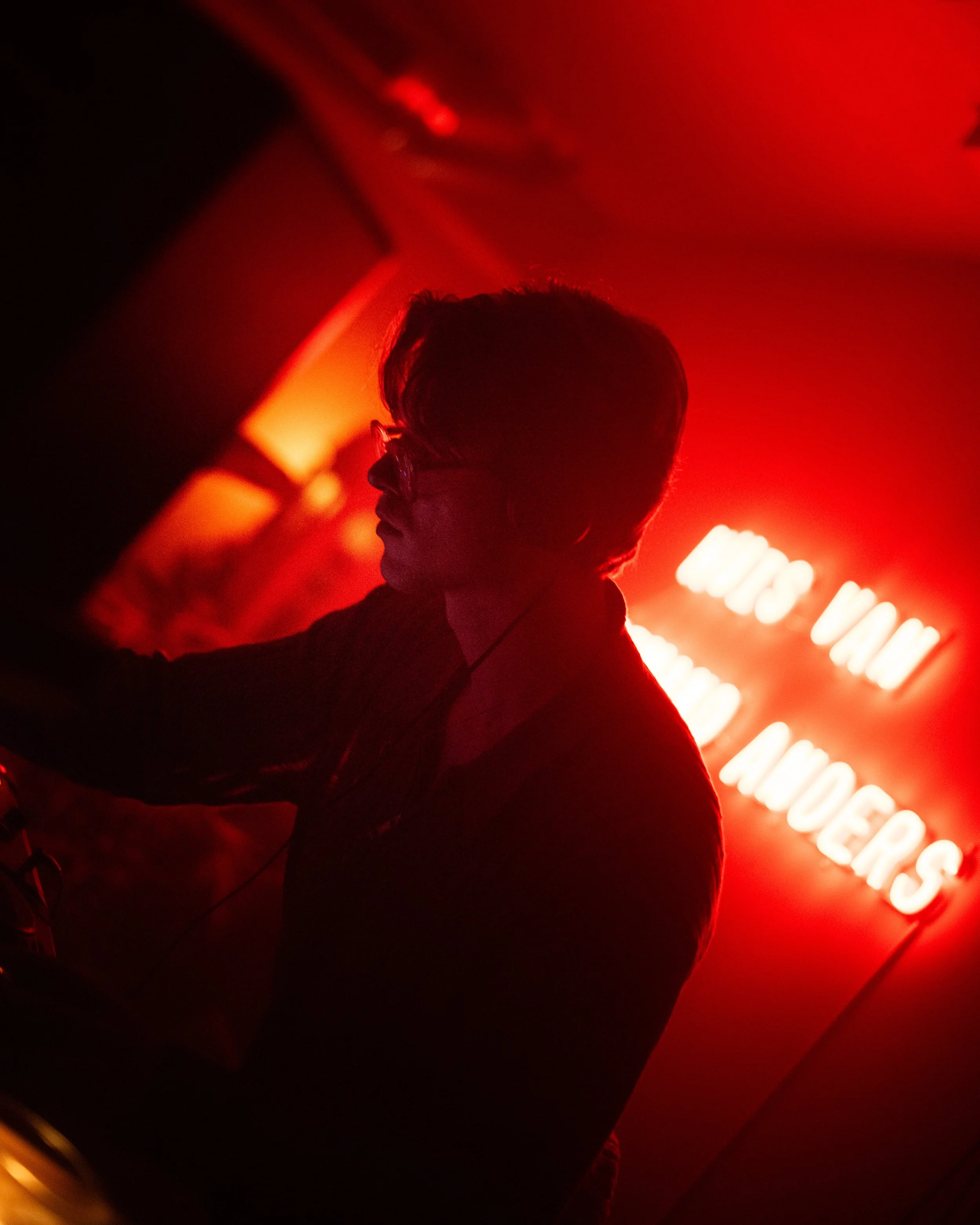 Silhouette of a person wearing headphones in a dimly lit room with red neon light.