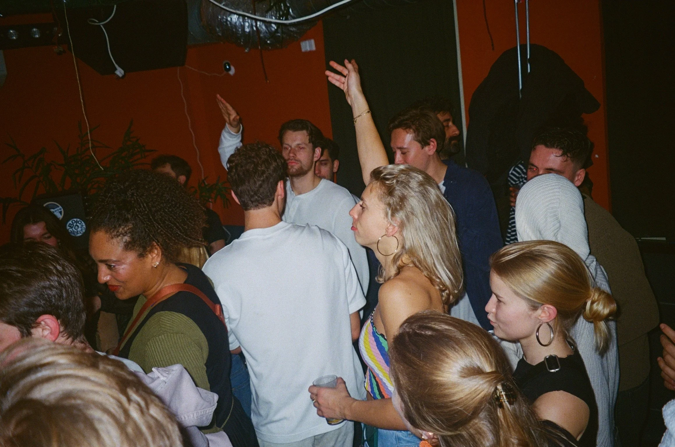 Crowd of people dancing at a party with one person raising a hand in the air.