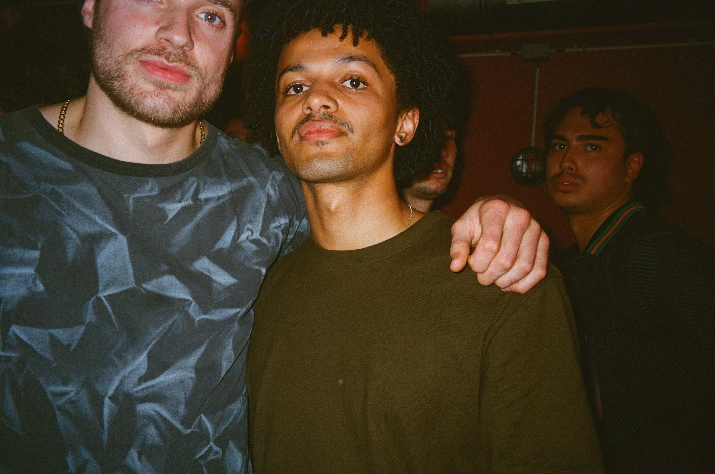 Three people standing together at a nighttime event; one person has an arm around another.