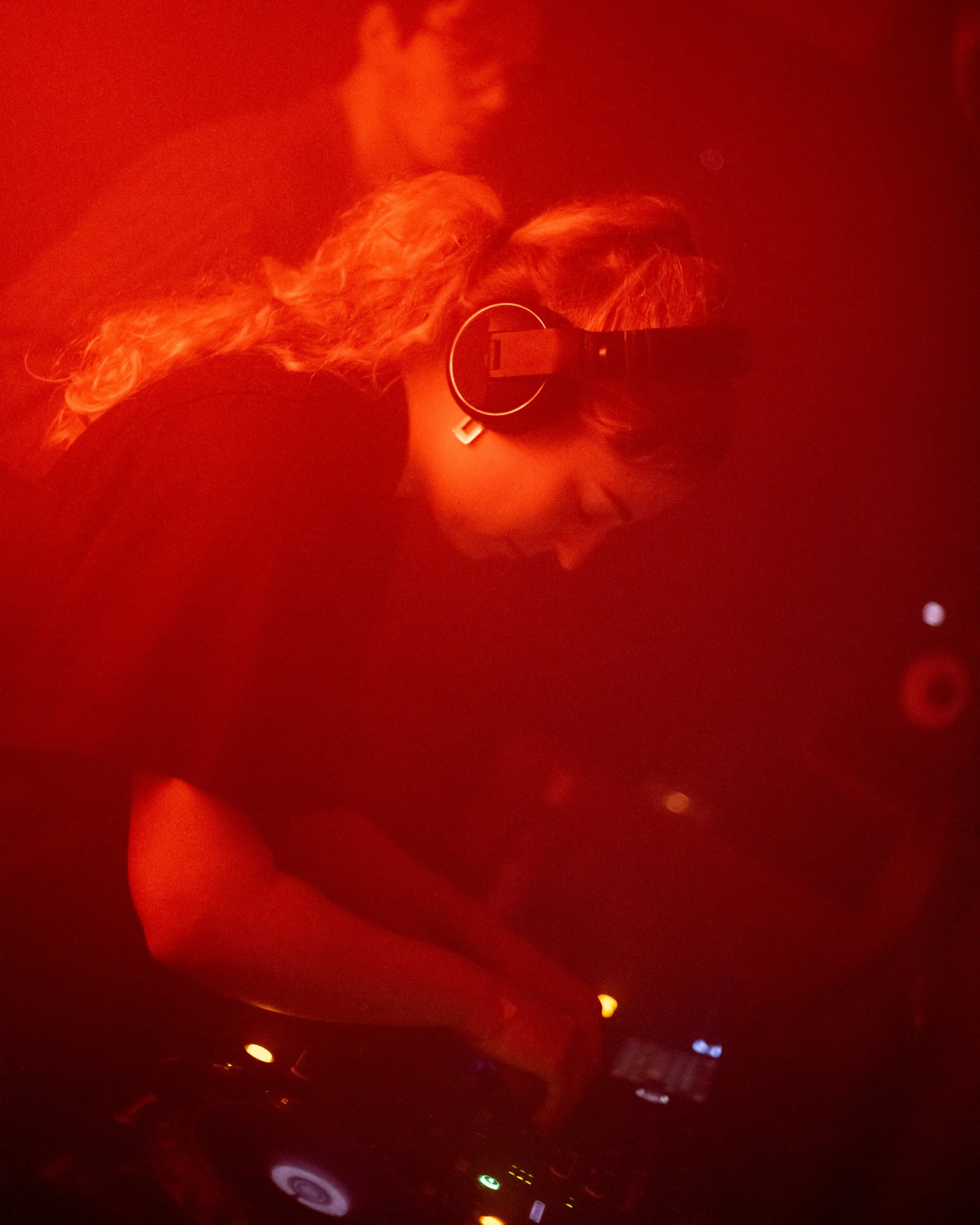 DJ wearing headphones mixing music on turntables in a dimly lit red environment