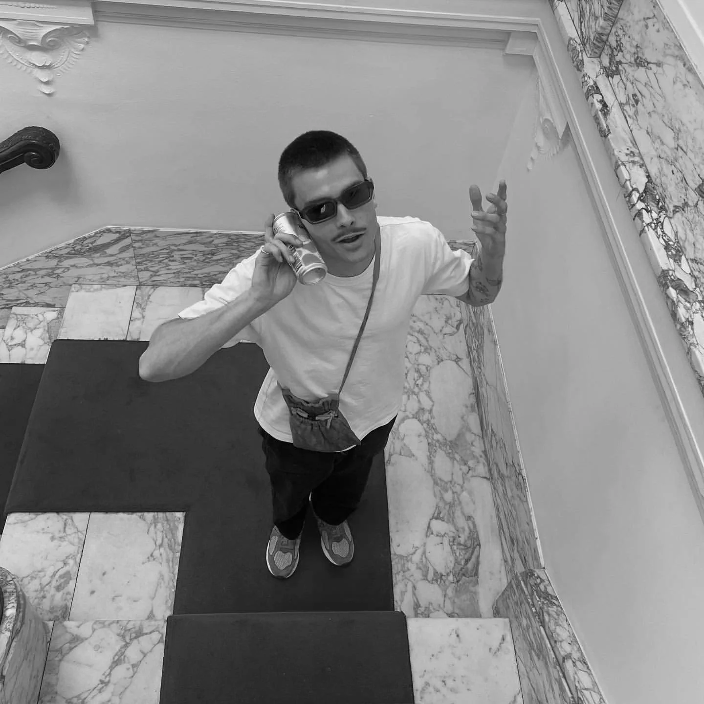Overhead view of person on stairs with sunglasses holding drink can and wearing crossbody bag