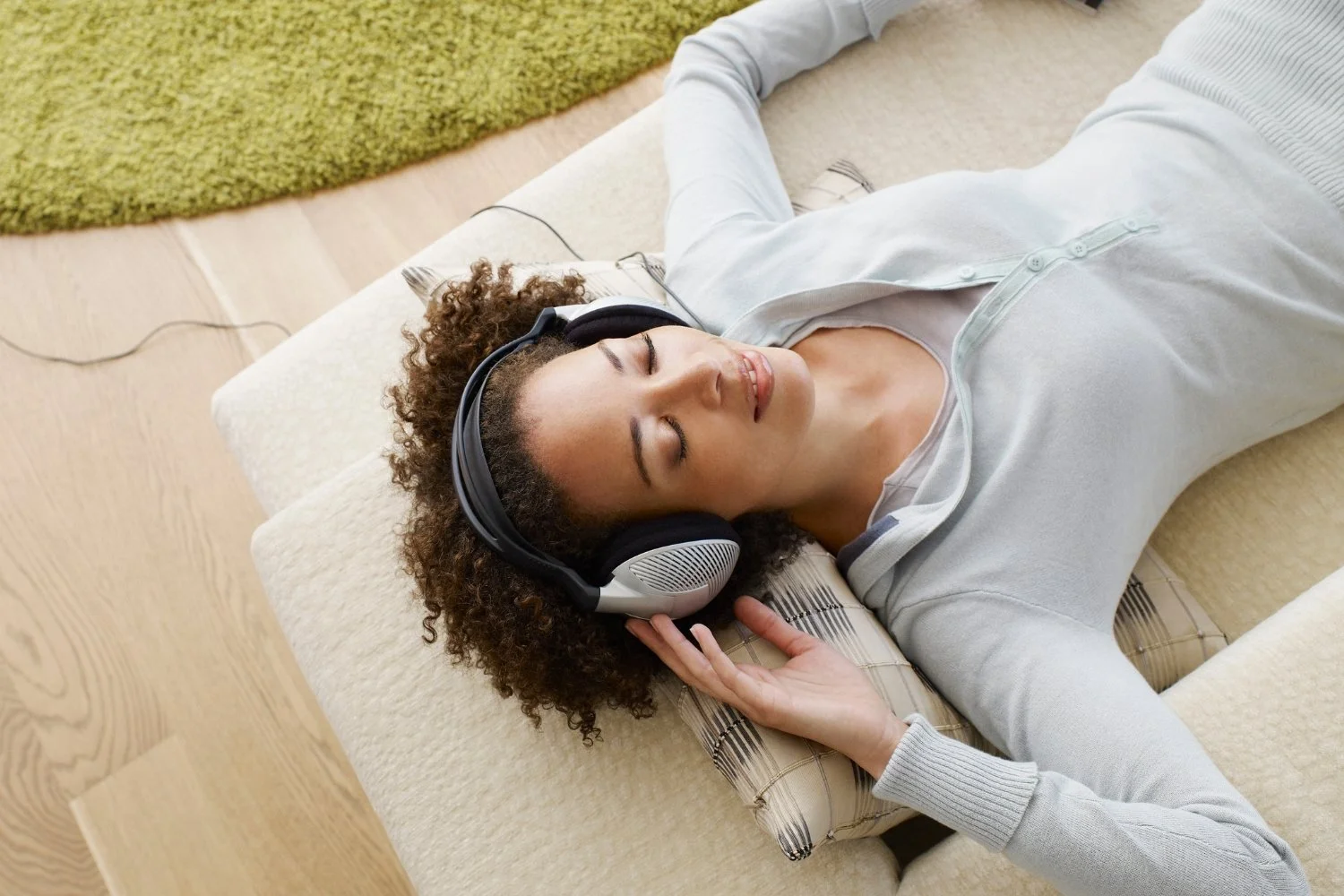 Frau liegt mit Kopfhörern und geschlossenen Augen entspannt auf dem Sofa.