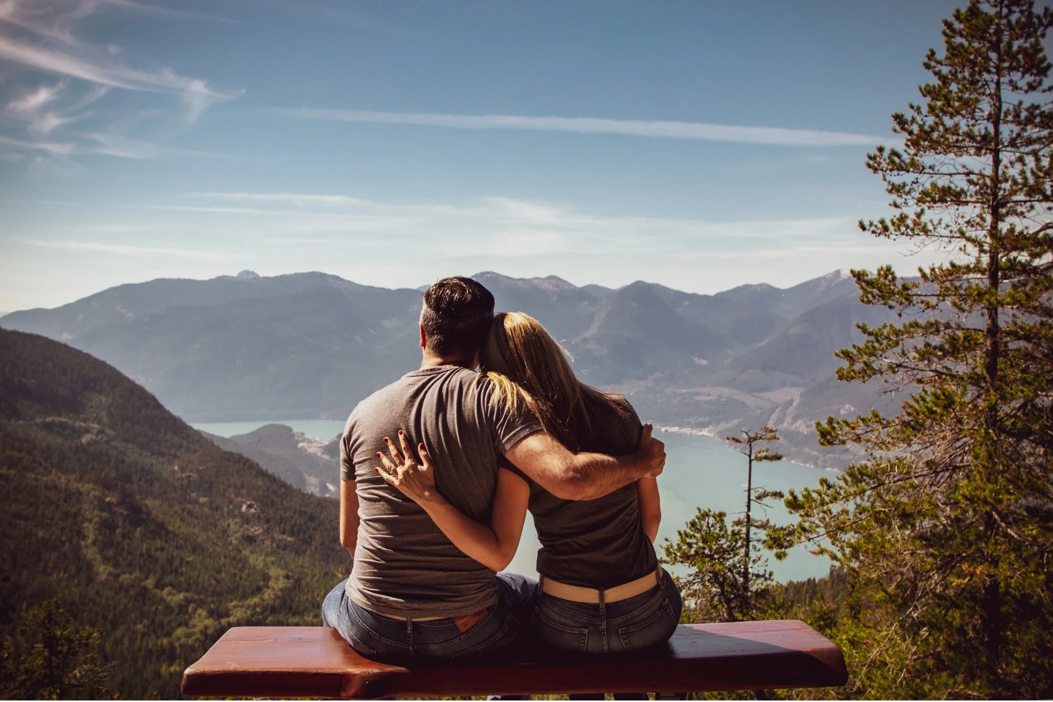 Paar sitzt Arm in Arm auf einer Bank mit einem Ausblick auf einem See.