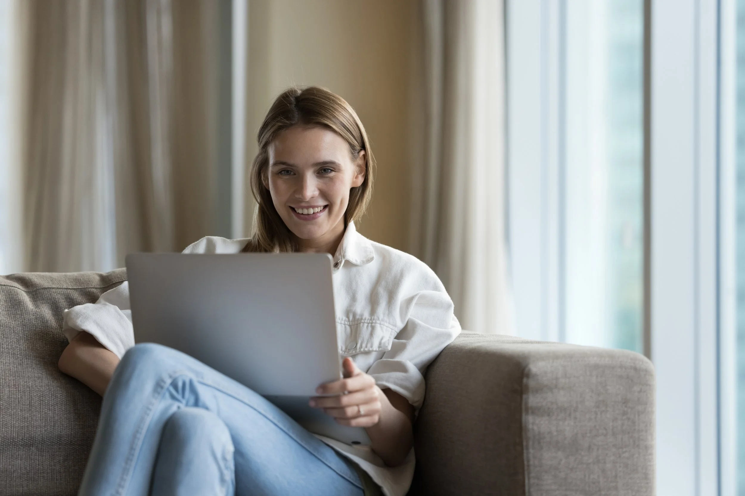 Frau sitzt auf dem Sofa mit Laptop und lächelt.