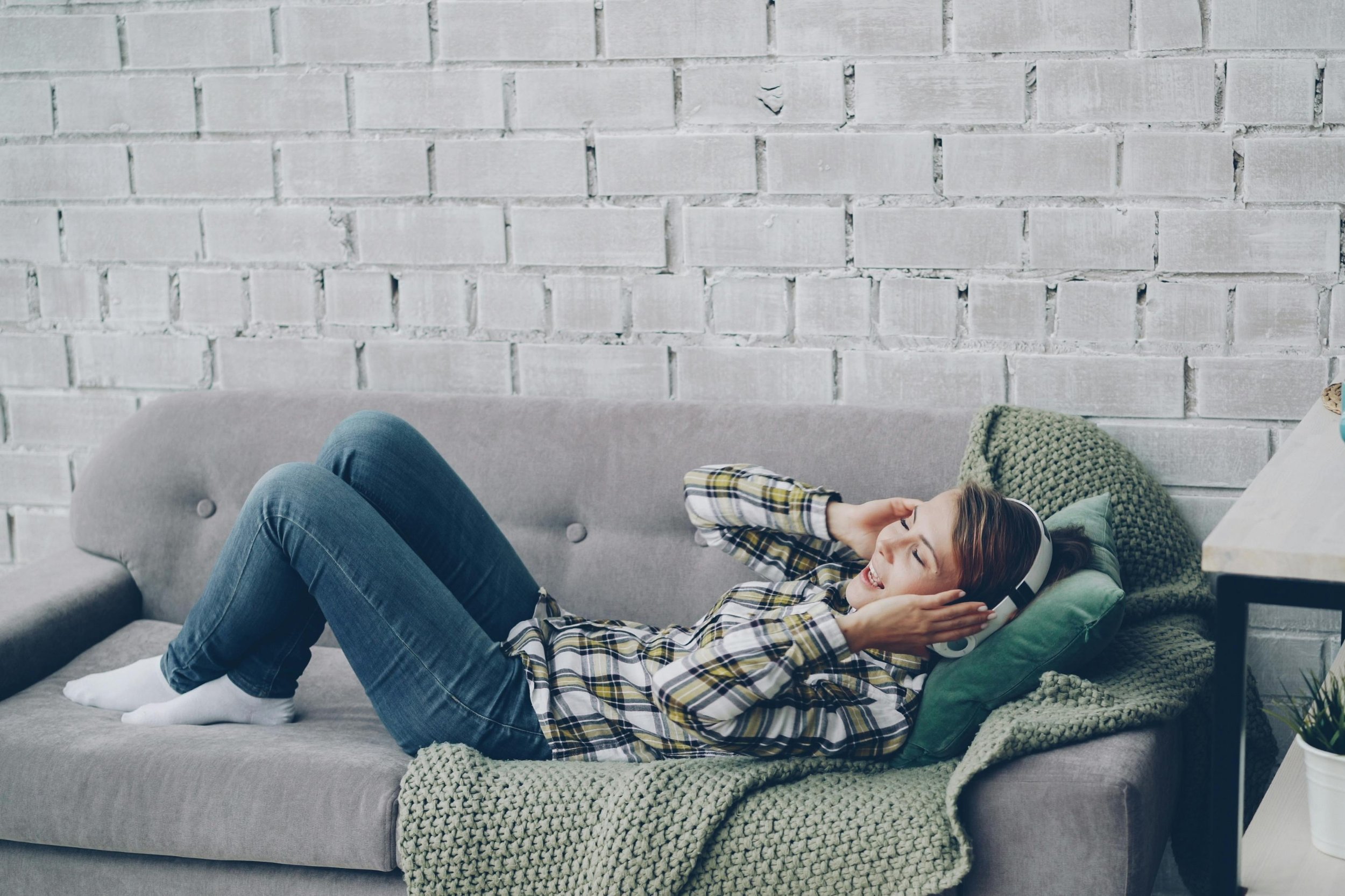 Frau liegt auf der Couch mit Kopfhörer und lächelt.