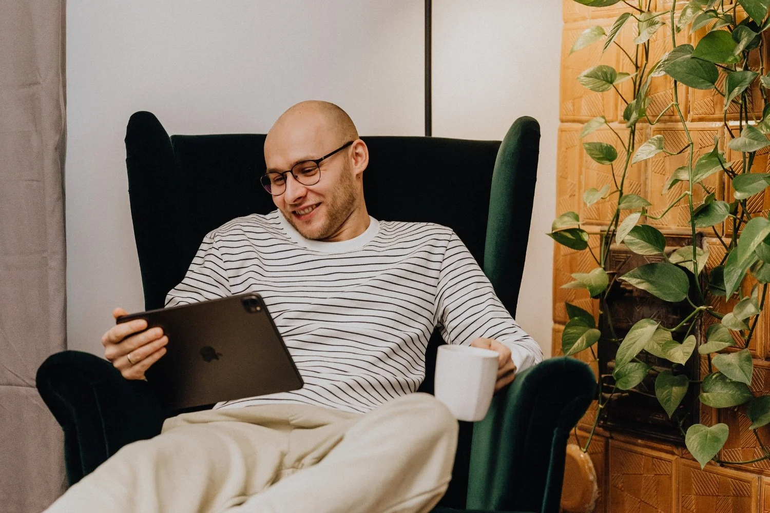 Mann sitzt im Sessel mit einer Tasse in der Hand und in der anderen Hand hält er ein Tablet.