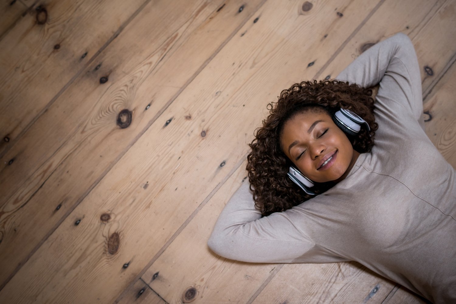 Frau liegt auf dem Boden und hört eine Hypnose über Kopfhörer.